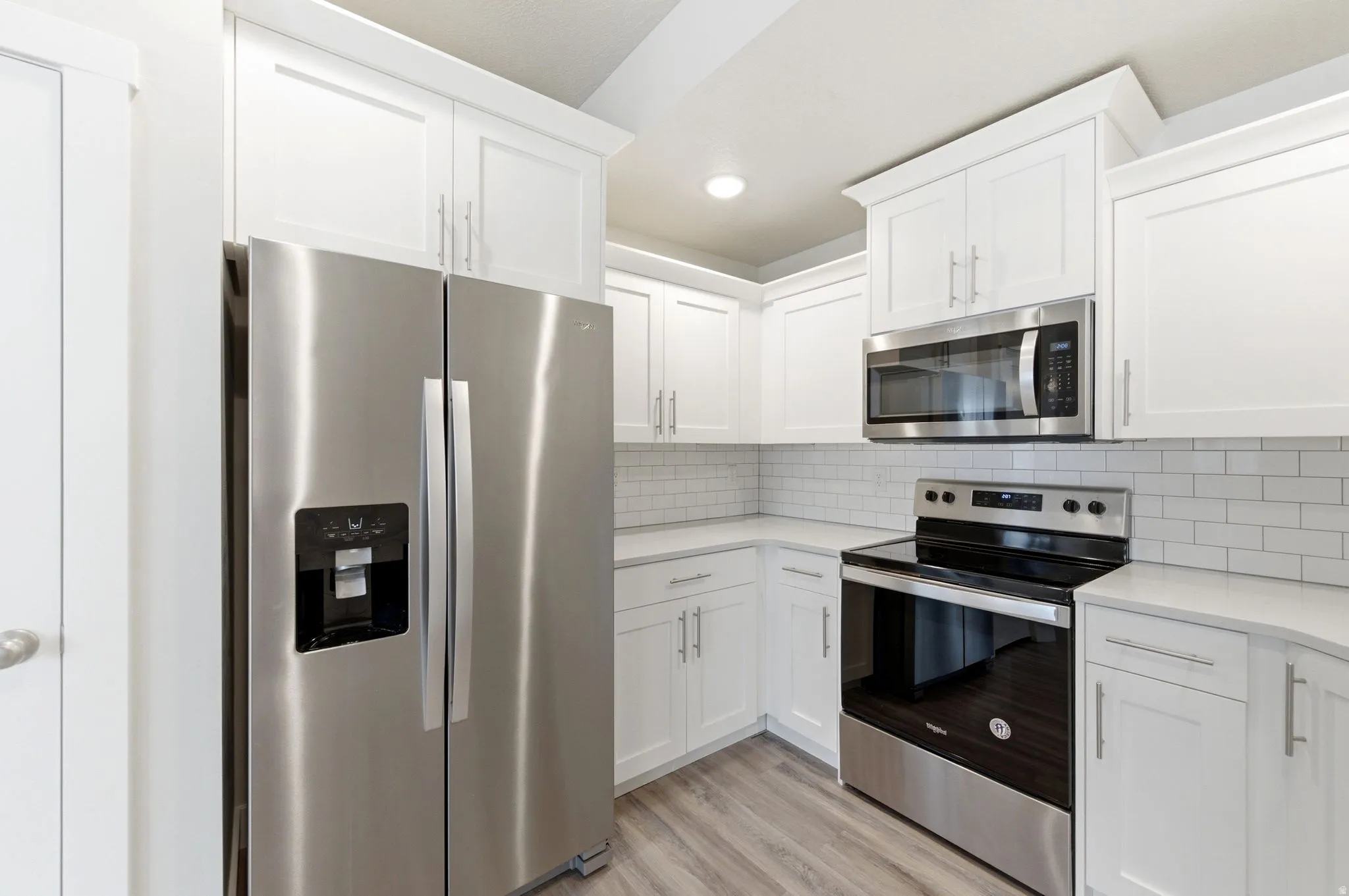 Kitchen featuring stainless steel appliances, white cabinets, light wood finished floors, recessed lighting, and backsplash