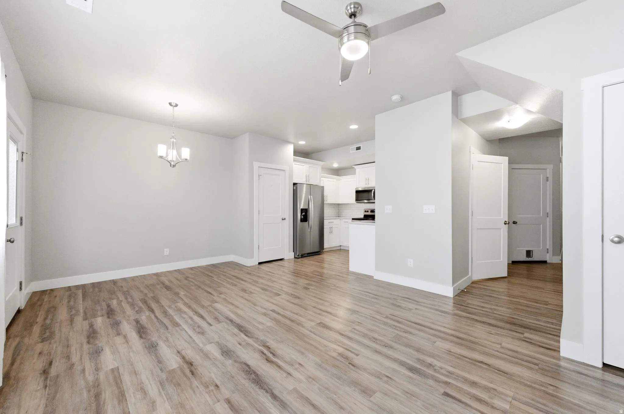 Unfurnished living room featuring a ceiling fan, hanging lights, and light wood-style floors