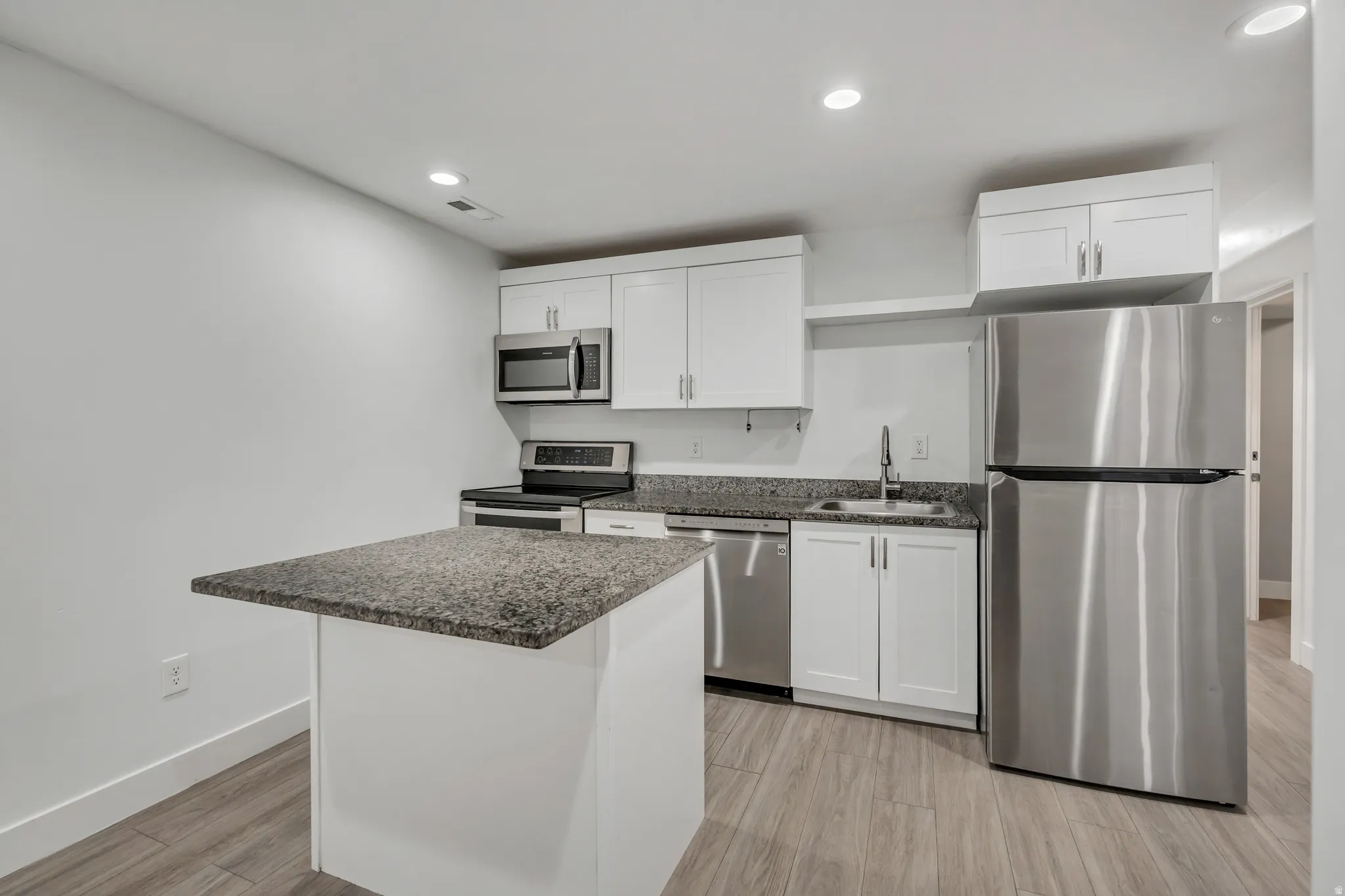 Kitchen with stainless steel appliances, white cabinetry, light wood finished floors, recessed lighting, and a kitchen island