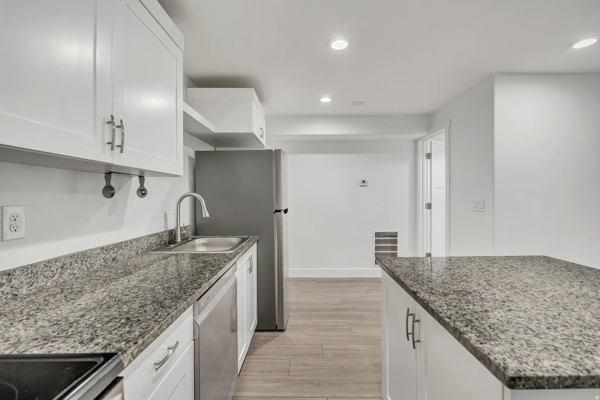 Kitchen with white cabinets, recessed lighting, stainless steel appliances, dark stone counters, and wood tiled floors