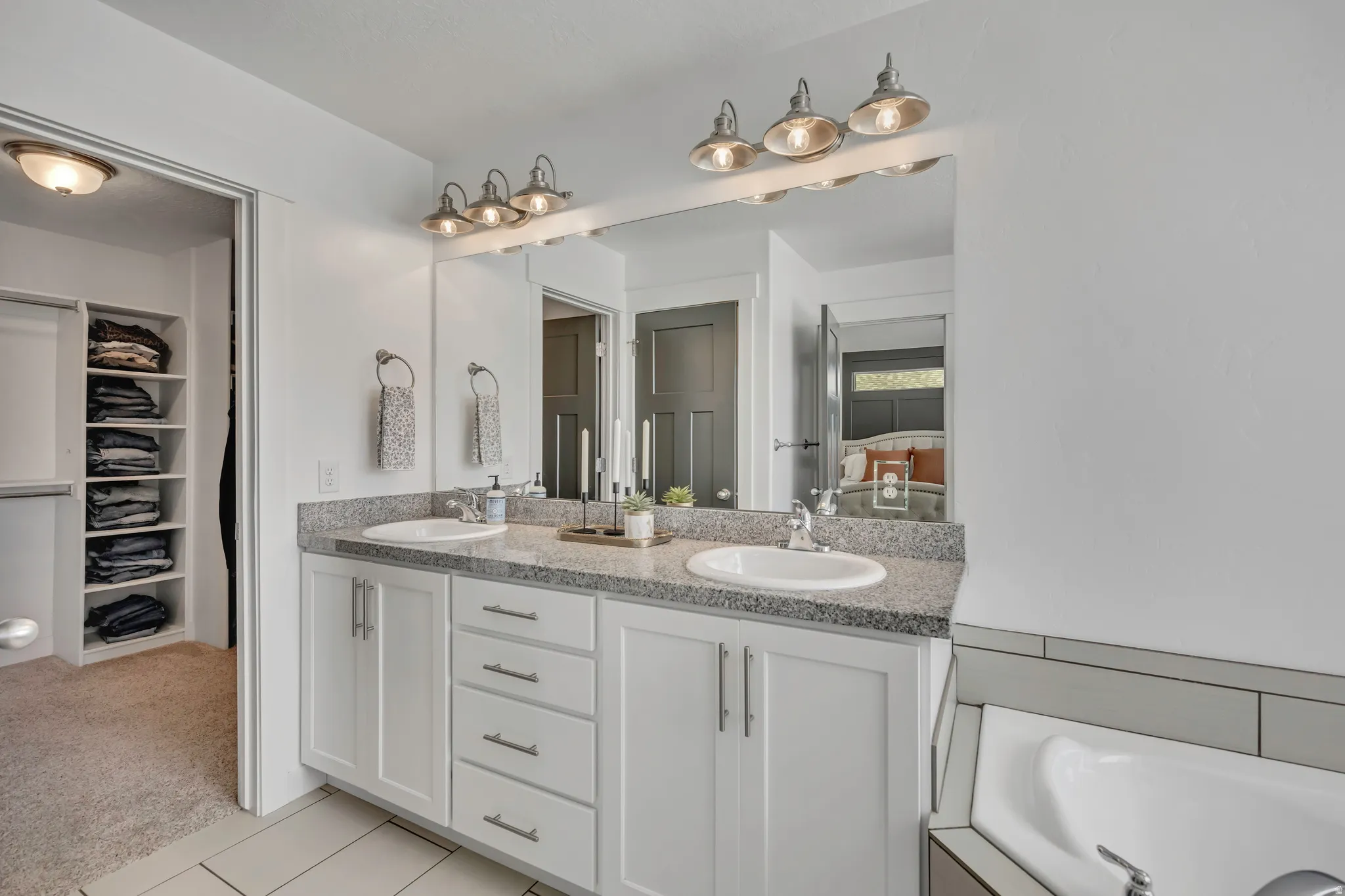 Bathroom with double vanity, light colored carpet, a spacious closet, light tile patterned flooring, and ensuite bathroom
