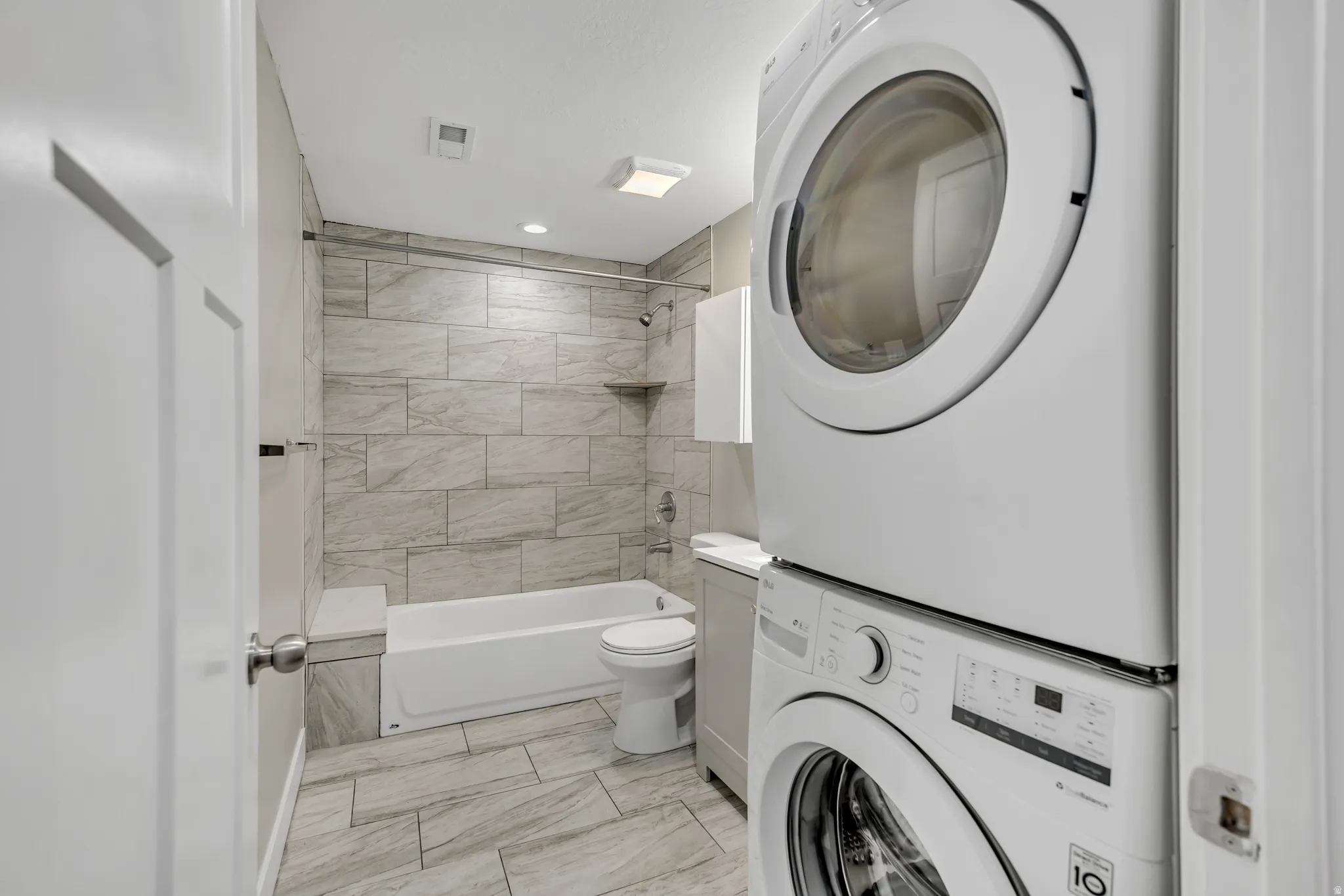 Bathroom featuring  shower combination, stacked washer / dryer, and light marble finish floors