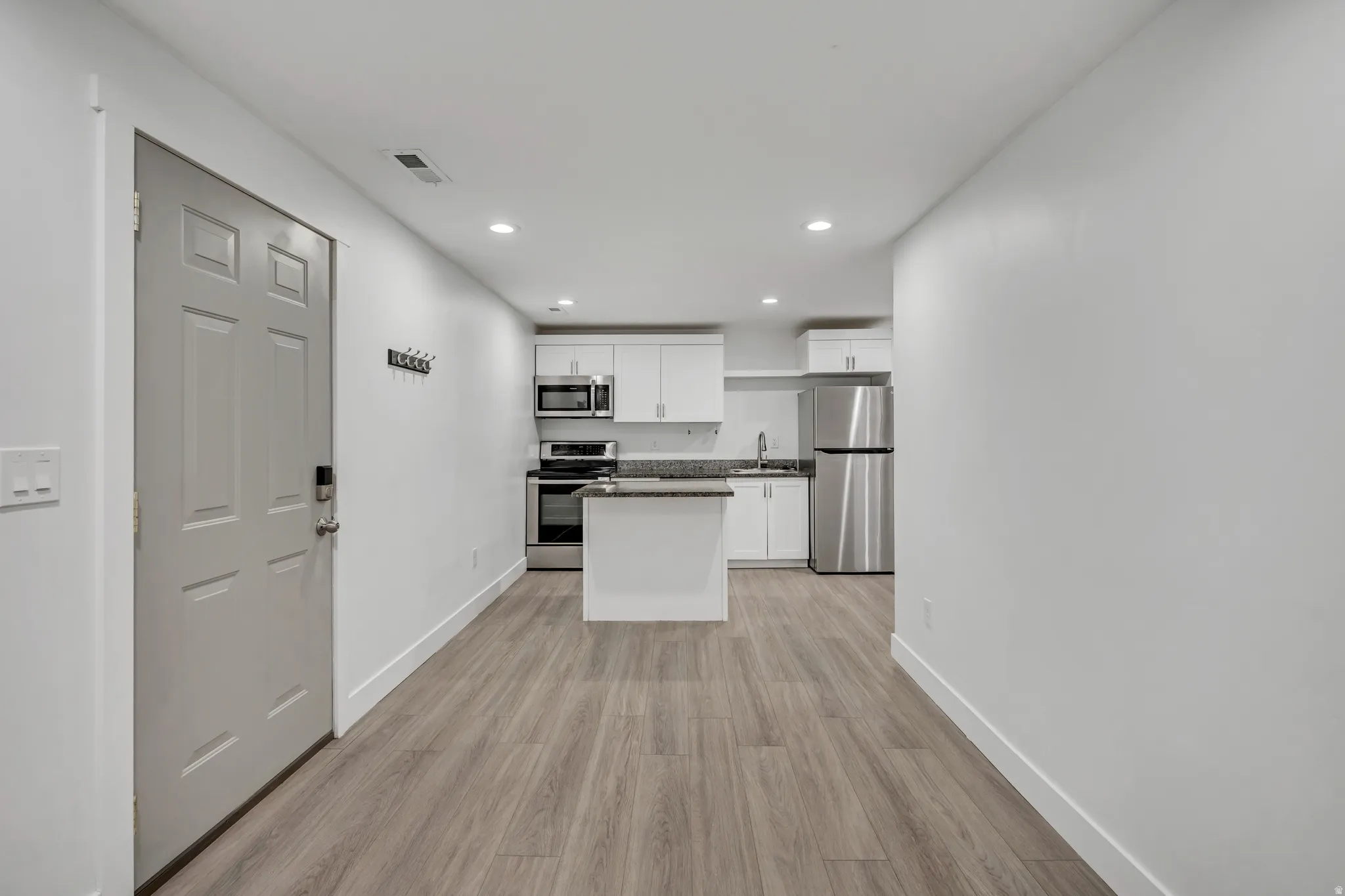 Kitchen featuring white cabinetry, stainless steel appliances, light wood-style flooring, recessed lighting, and a center island