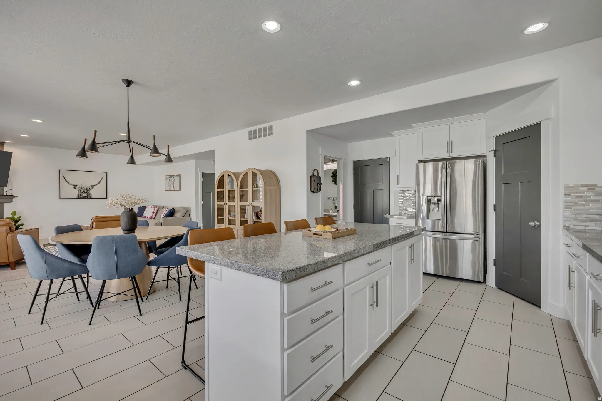 Kitchen featuring white cabinetry, a kitchen breakfast bar, stainless steel fridge, light stone countertops, and a kitchen island