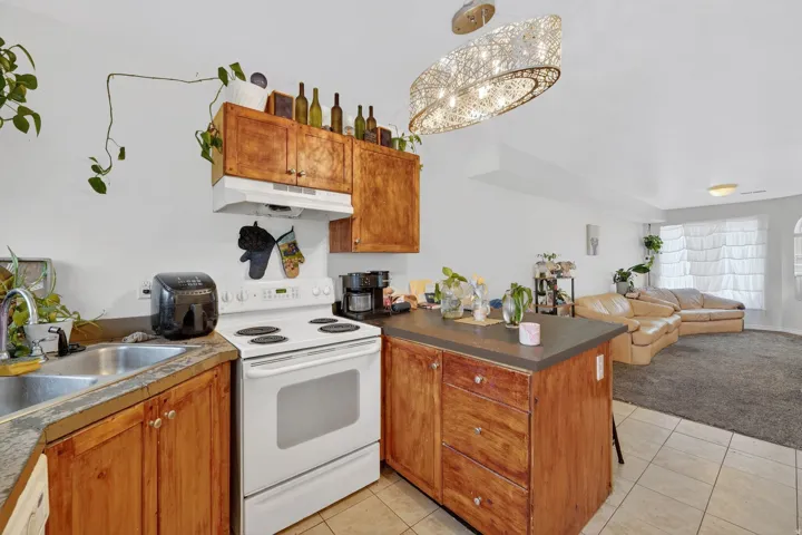 Kitchen with white range with electric stovetop, a peninsula, open floor plan, wood finish cabinetry, and light tile patterned floors