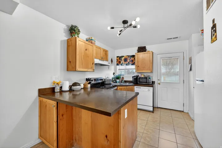 Kitchen with a peninsula, stainless steel appliances, dark countertops, light tile patterned floors, and light wood finish cabinets