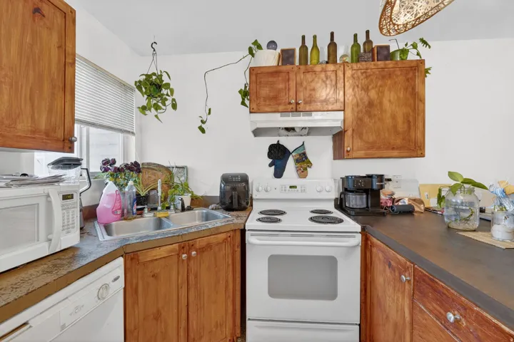 Kitchen featuring white appliances, wood finish cabinetry, and dark countertops