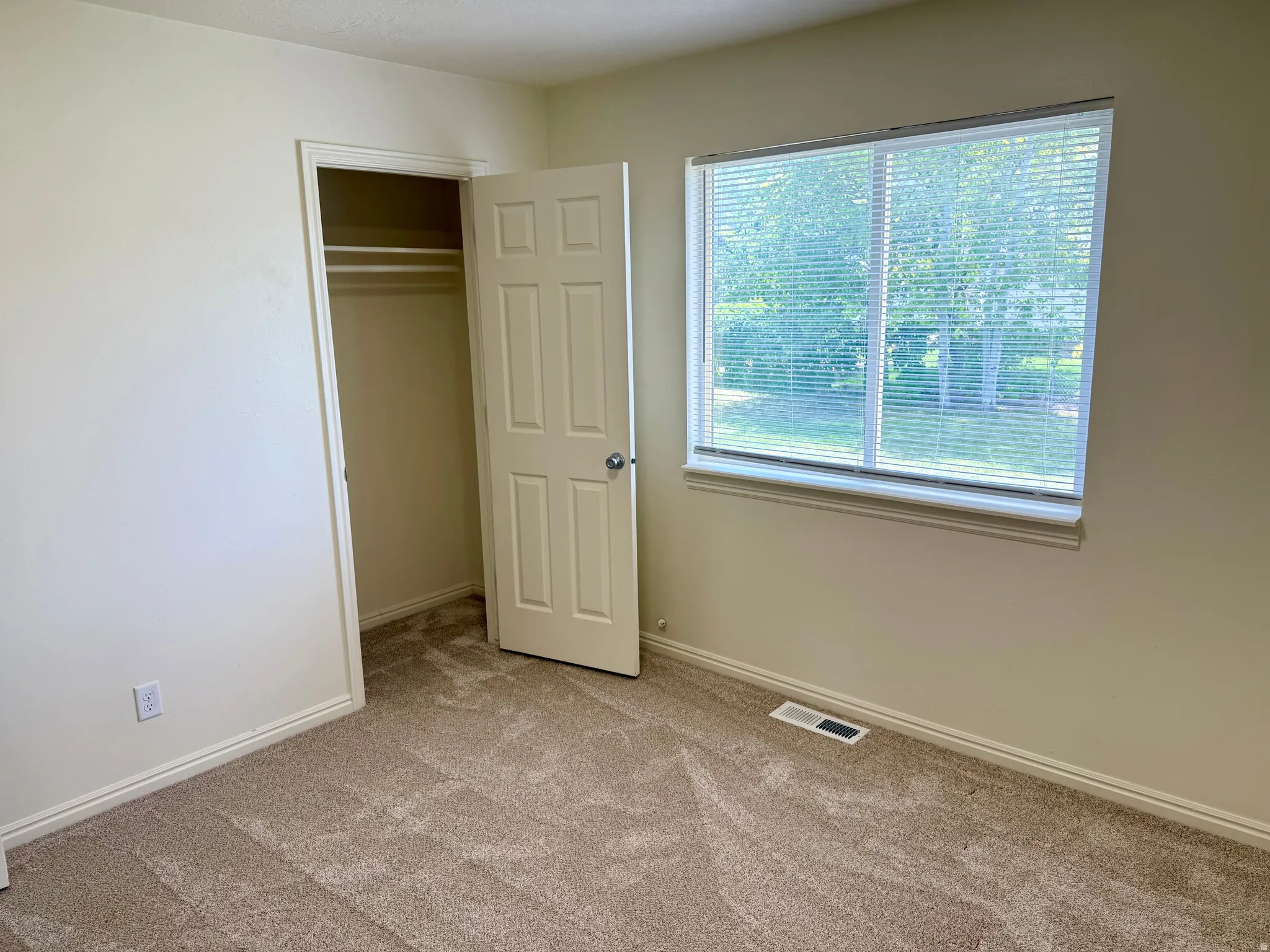 Room featuring neutral-toned walls, textured carpeting, and a window with horizontal blinds