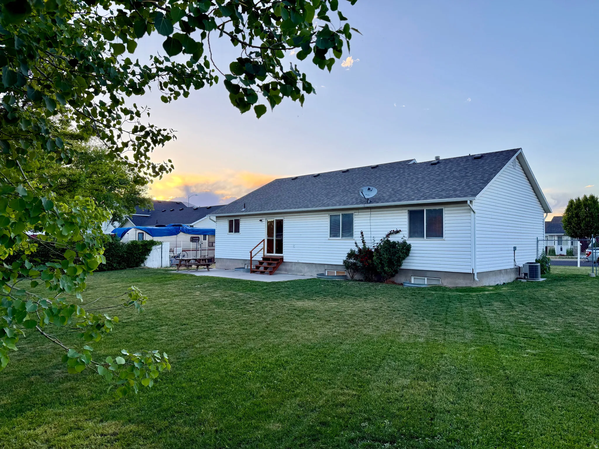 Expansive rear yard featuring a large green lawn, a concrete patio, and a wood deck with stairs