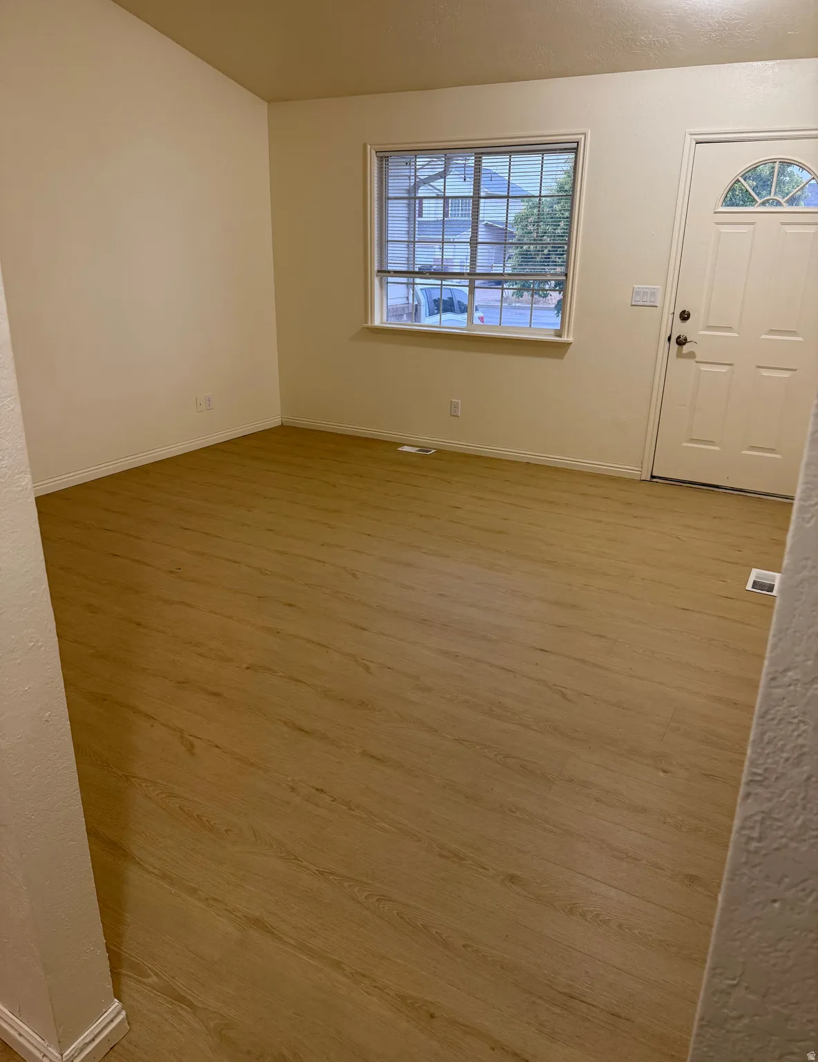 Spacious room featuring light wood-finish flooring, neutral wall tones, and a multi-pane window with blinds