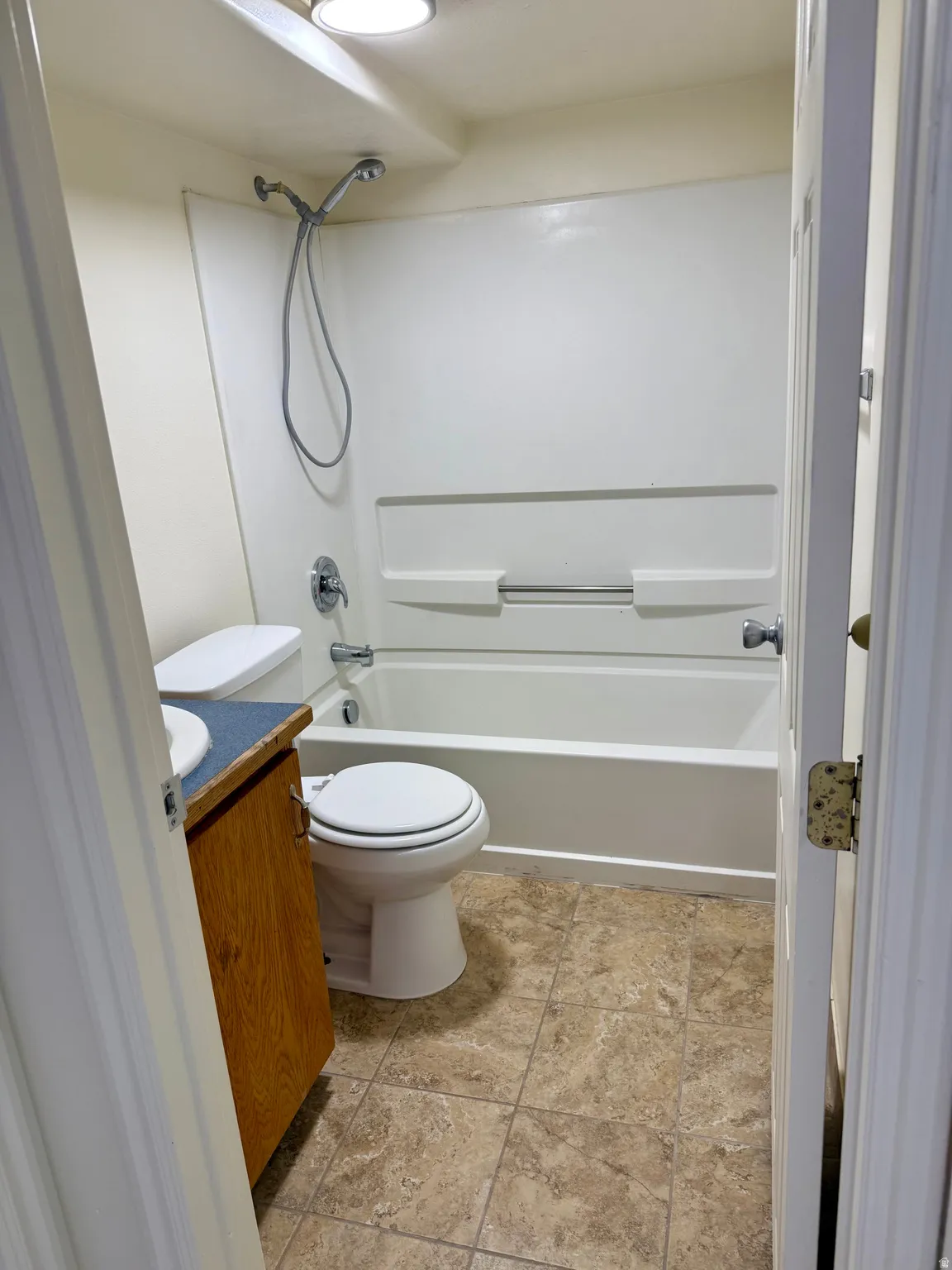 Full bathroom featuring a tub/shower combination with a white surround, toilet, and a vanity with a wood-finish cabinet, light blue countertop, and integrated sink