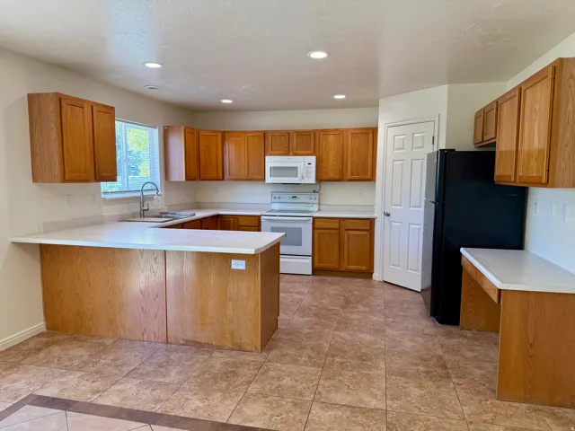 U-shaped kitchen featuring wood-finish cabinetry, light-toned countertops, and tile flooring