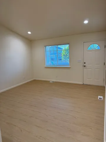 Interior space featuring light wood-finish flooring, recessed ceiling lighting, a window with exterior views, and a white paneled entry door with an arched glass insert