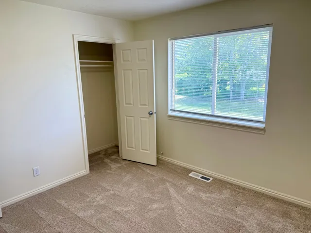 Room featuring neutral-toned walls, textured carpeting, and a window with horizontal blinds