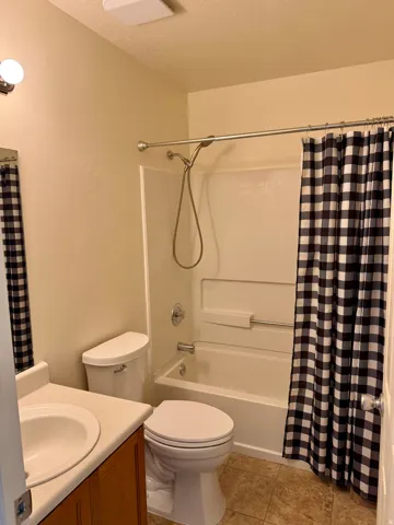 Full bathroom featuring a white bathtub and shower combination with a curved shower rod, a white toilet, and a vanity with an integrated sink and wood-finish cabinetry