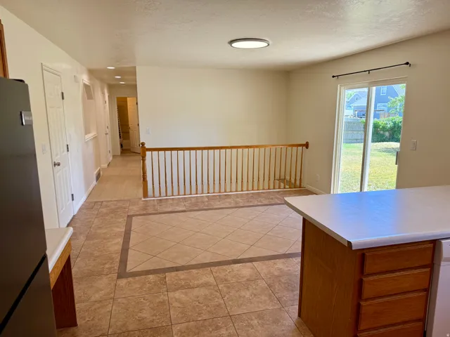 Kitchen and living area featuring tile flooring, wood-finish cabinetry, a white countertop, and sliding glass door access to the backyard
