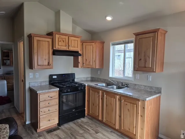 Kitchen with black gas range, light countertops, vaulted ceiling, and light wood-type flooring