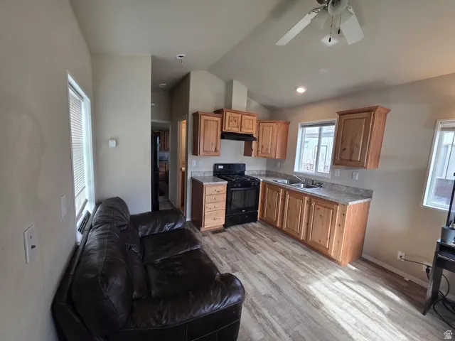 Kitchen featuring black gas range, light countertops, vaulted ceiling, a ceiling fan, and light wood-type flooring
