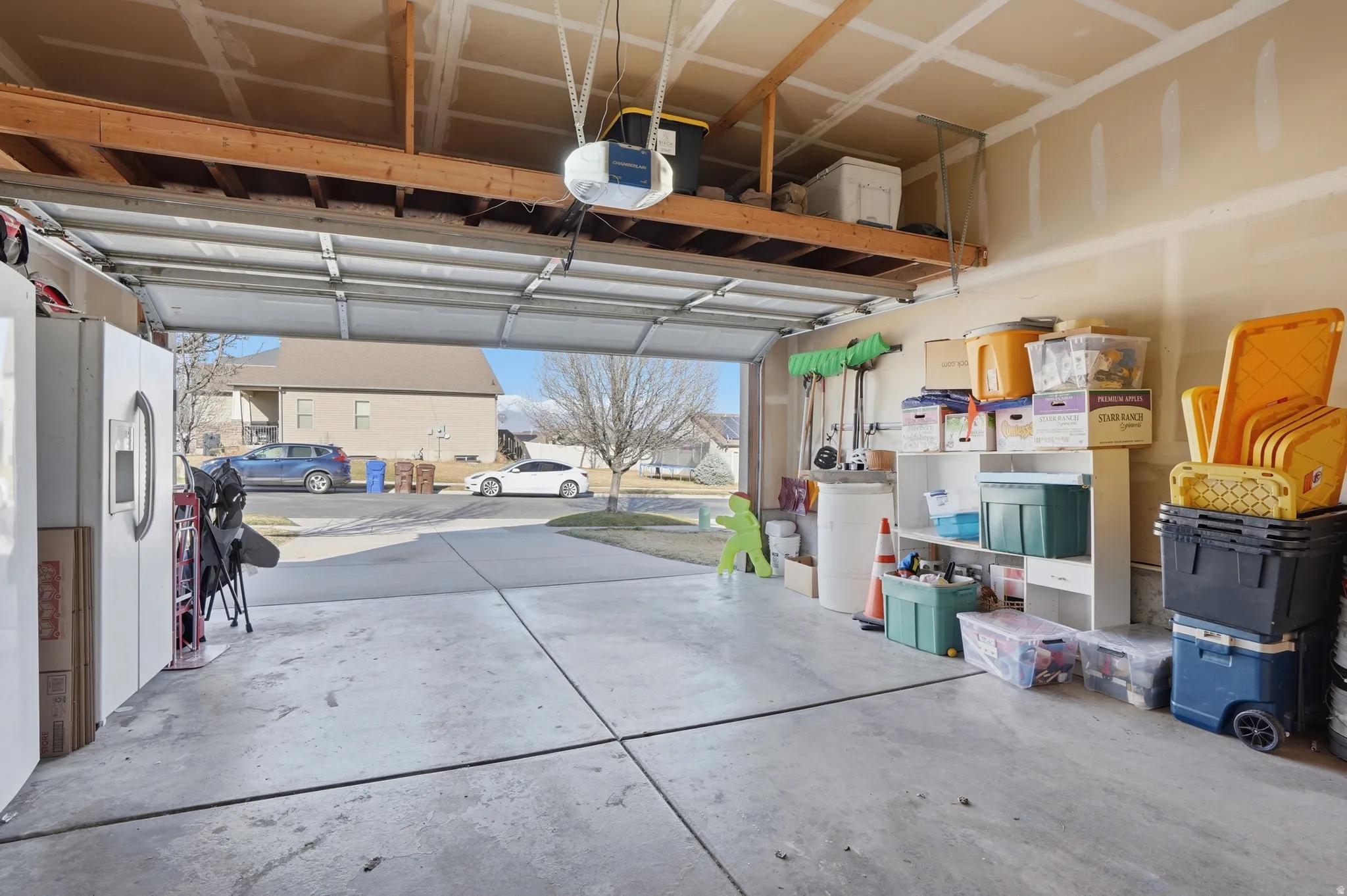 Garage featuring a residential view, white fridge with ice dispenser, and a garage door opener