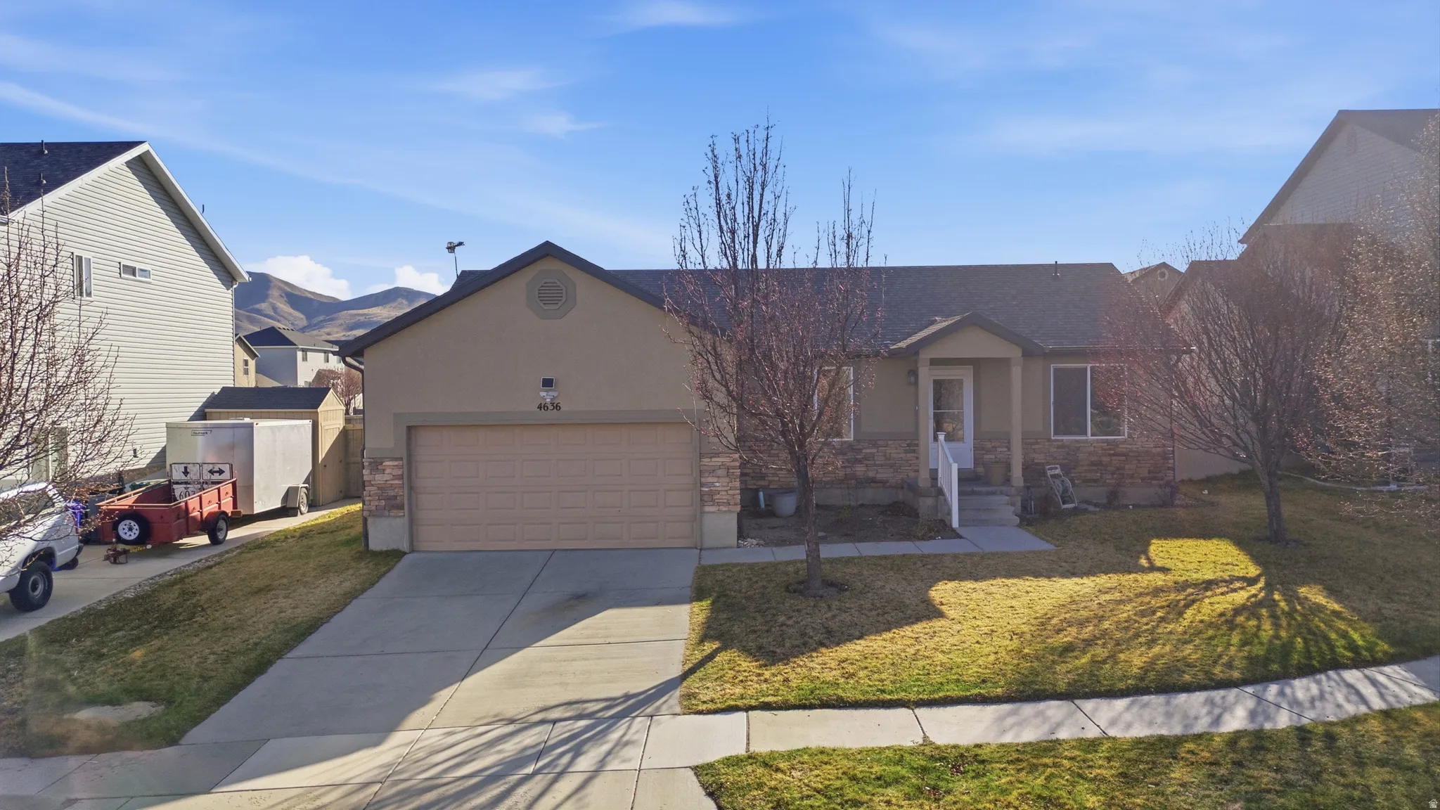 Ranch-style house with a front yard, concrete driveway, a garage, stucco siding, and stone siding