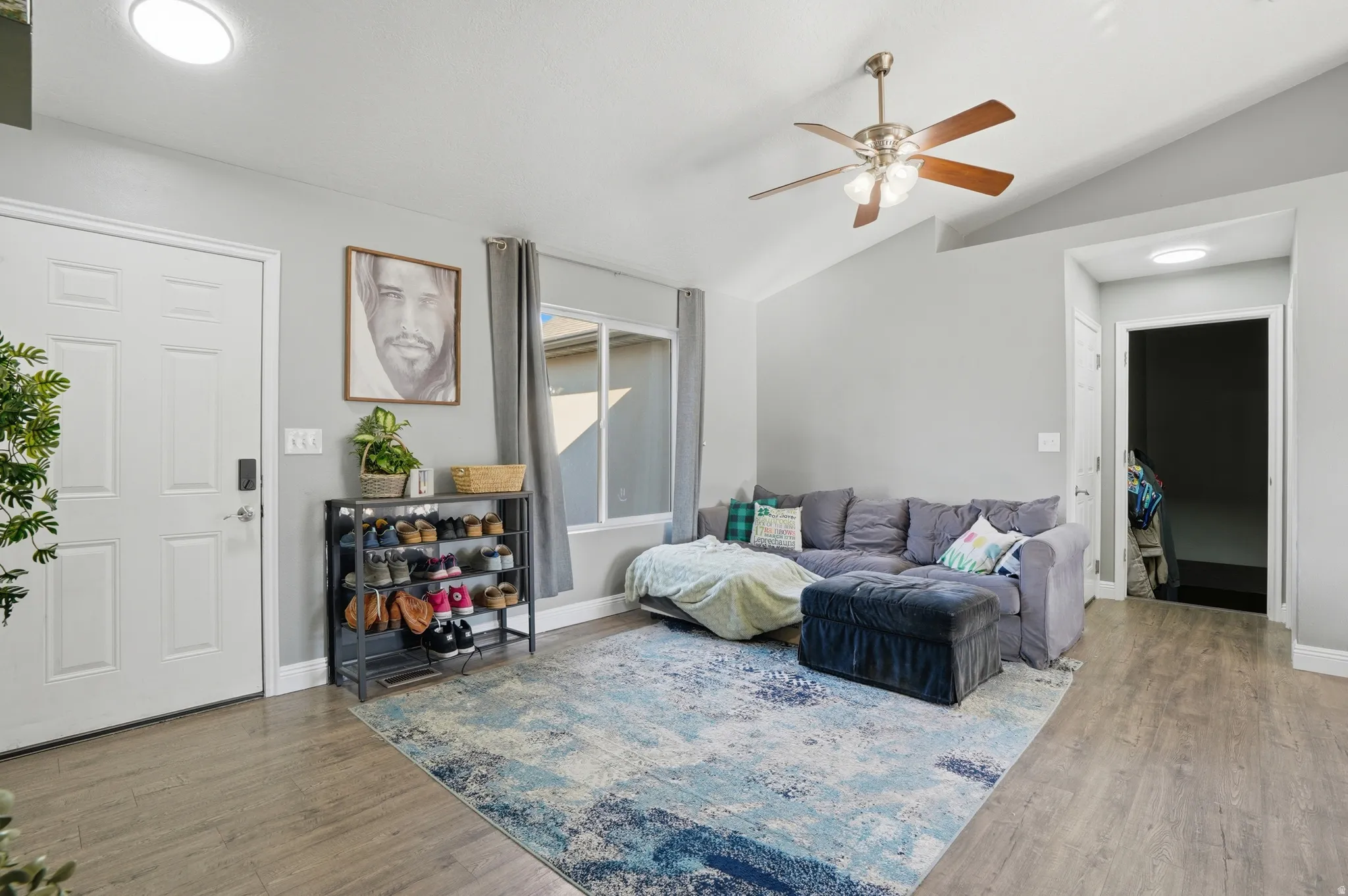 Living area featuring ceiling fan, light wood-style flooring, and lofted ceiling