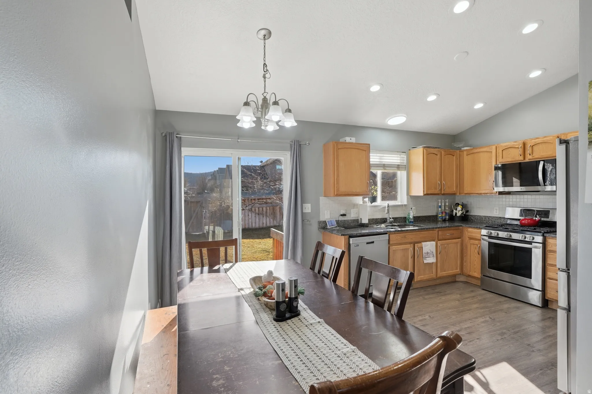 Kitchen featuring stainless steel appliances, backsplash, vaulted ceiling, dark wood-style floors, and hanging lights