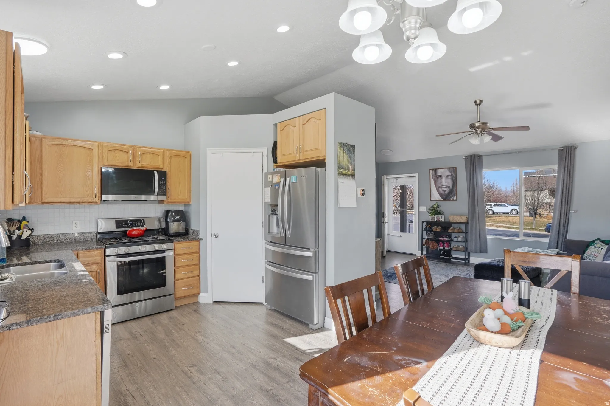 Kitchen with lofted ceiling, stainless steel appliances, light wood finish cabinets, light wood-style flooring, and ceiling fan