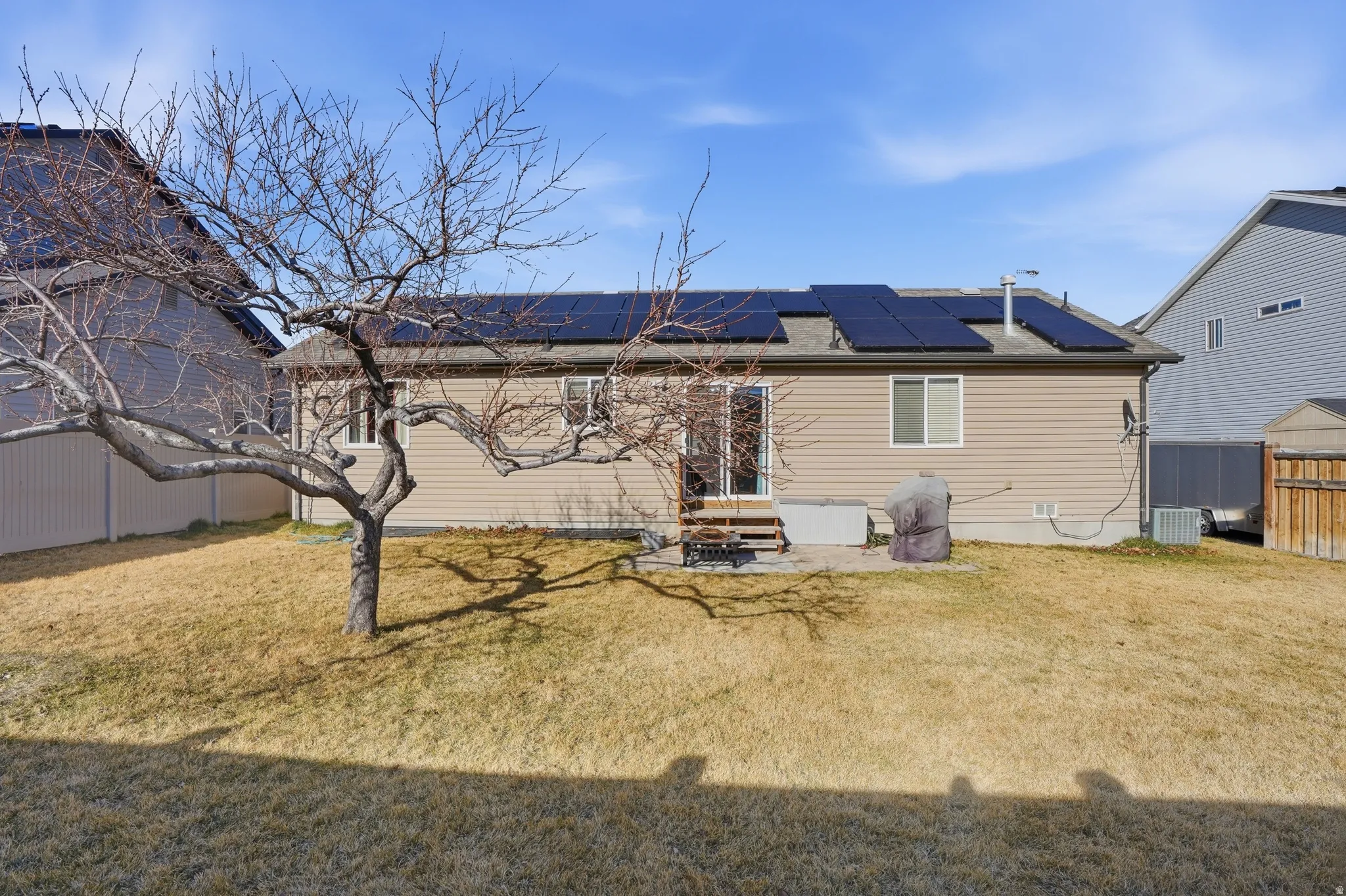 Rear view of house with roof mounted solar panels, a patio area, a yard, and a shingled roof