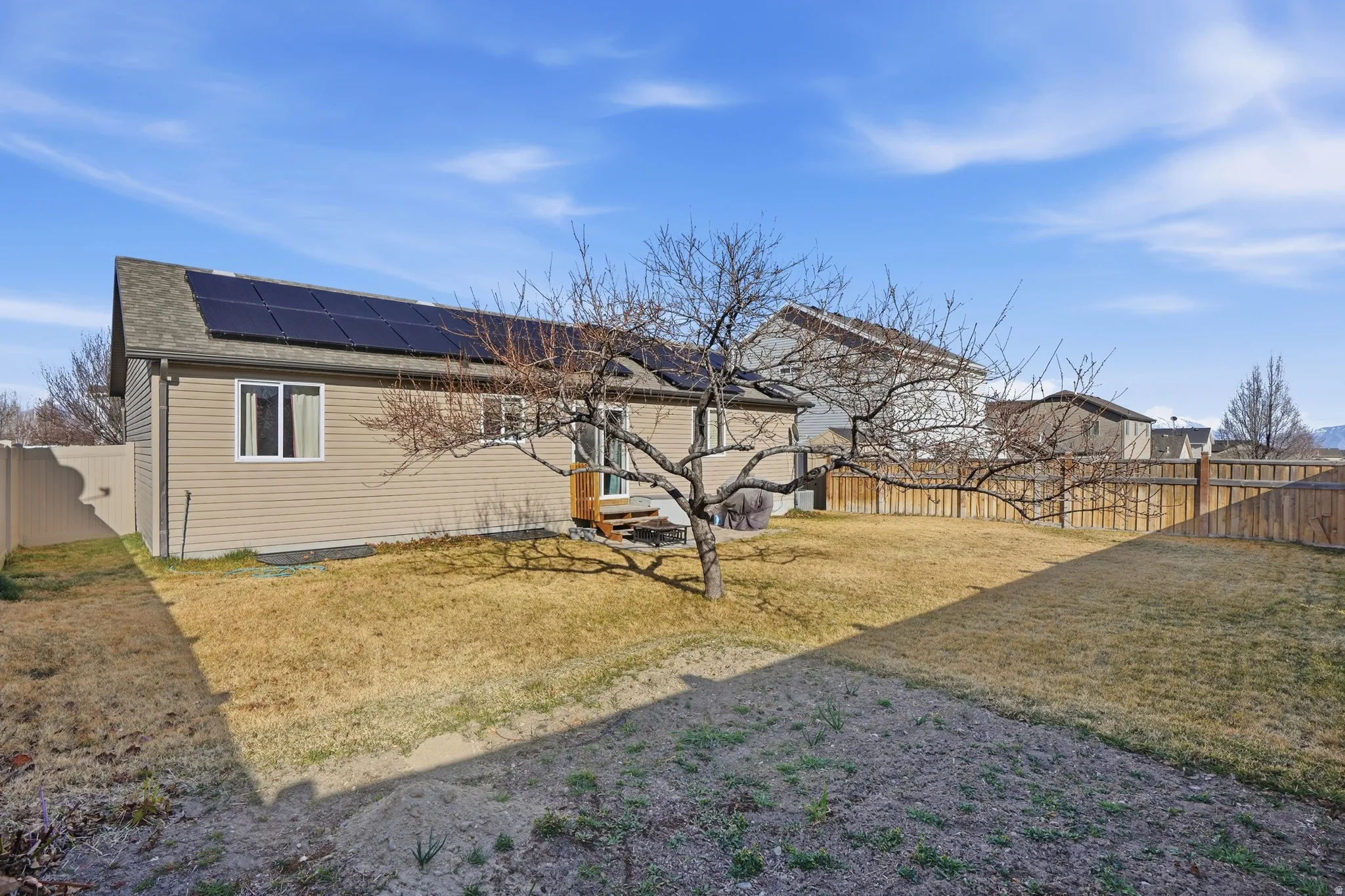 Rear view of house featuring a fenced backyard, roof mounted solar panels, and a shingled roof