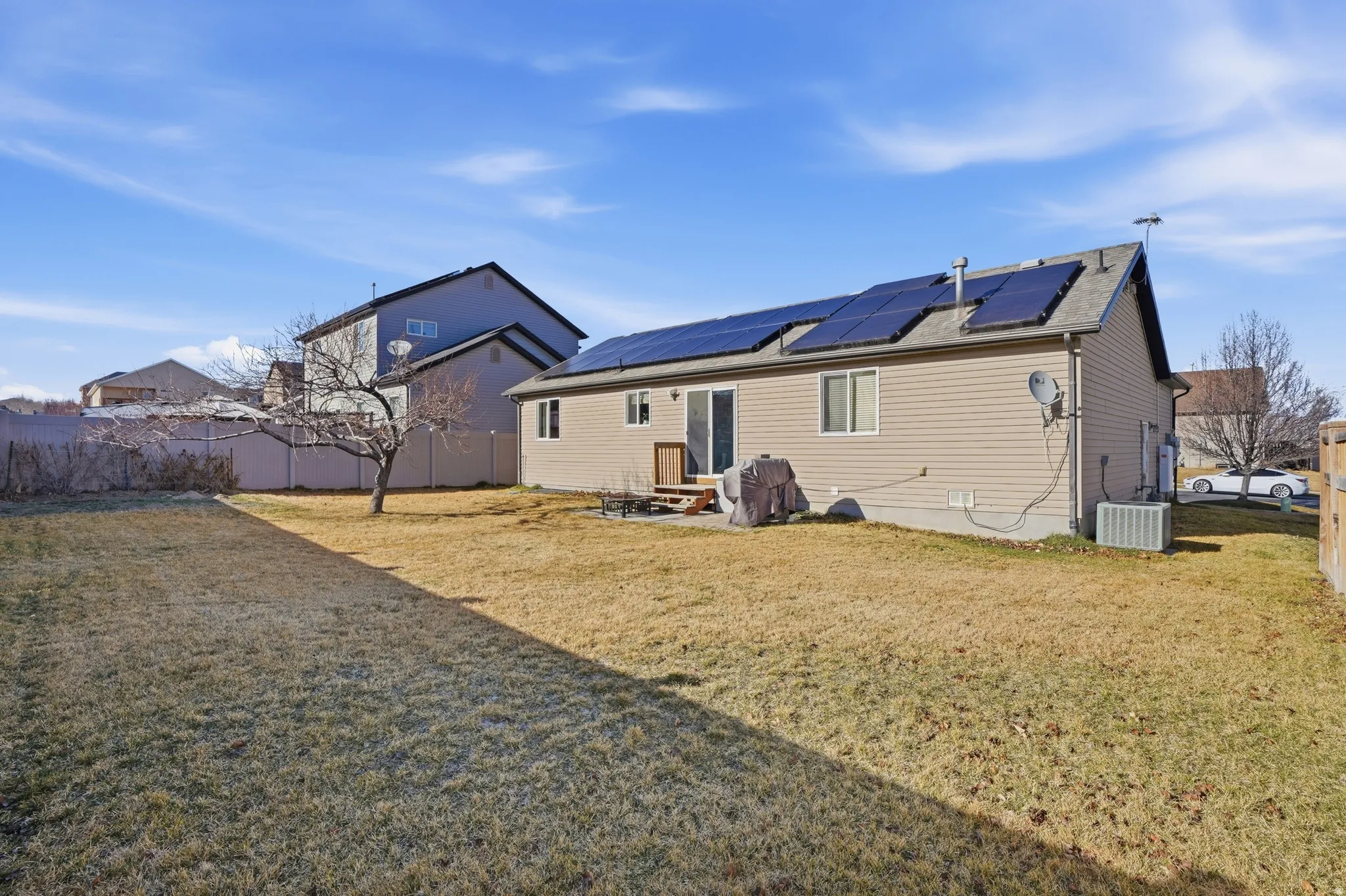 Rear view of house with roof mounted solar panels, a fenced backyard, and a patio