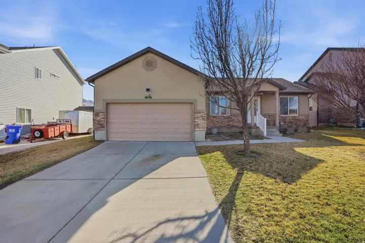 Ranch-style home featuring a front yard, concrete driveway, an attached garage, and stucco siding
