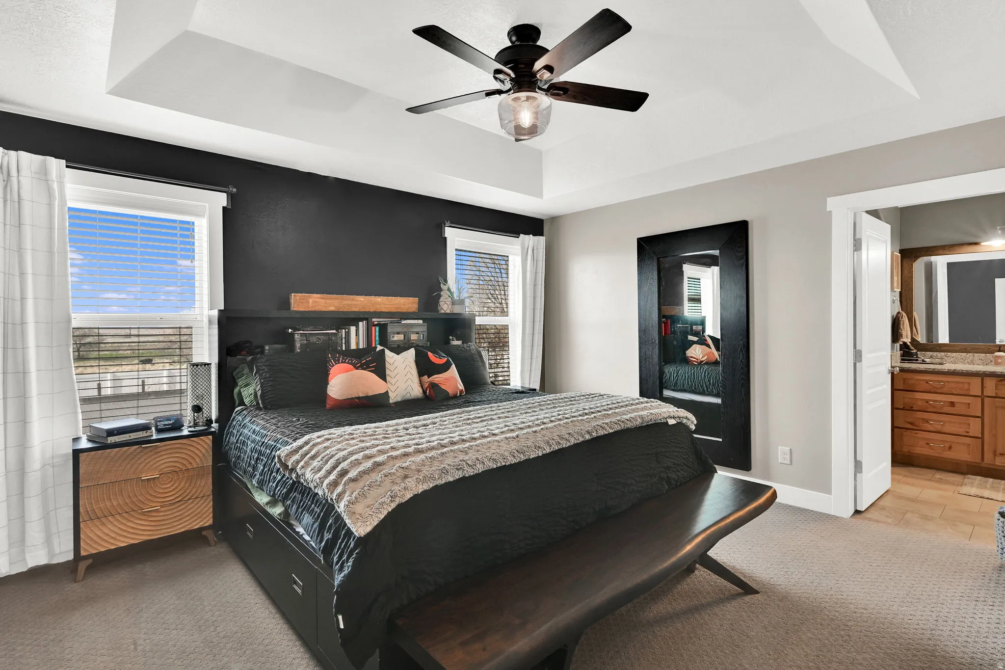 Bedroom featuring light carpet, a raised ceiling, ceiling fan, and ensuite bath