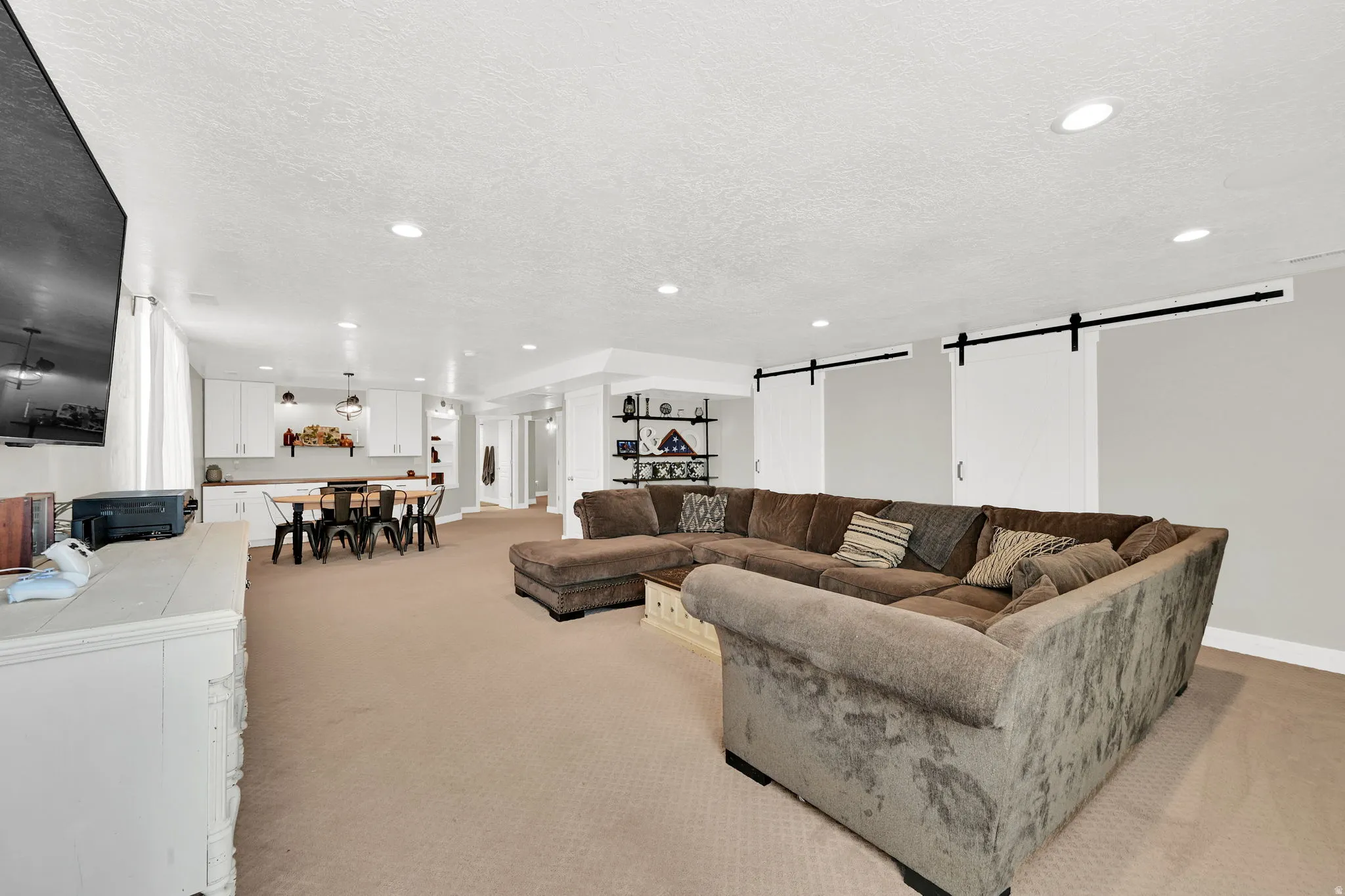 Living room featuring a barn door, light carpet, a textured ceiling, and recessed lighting