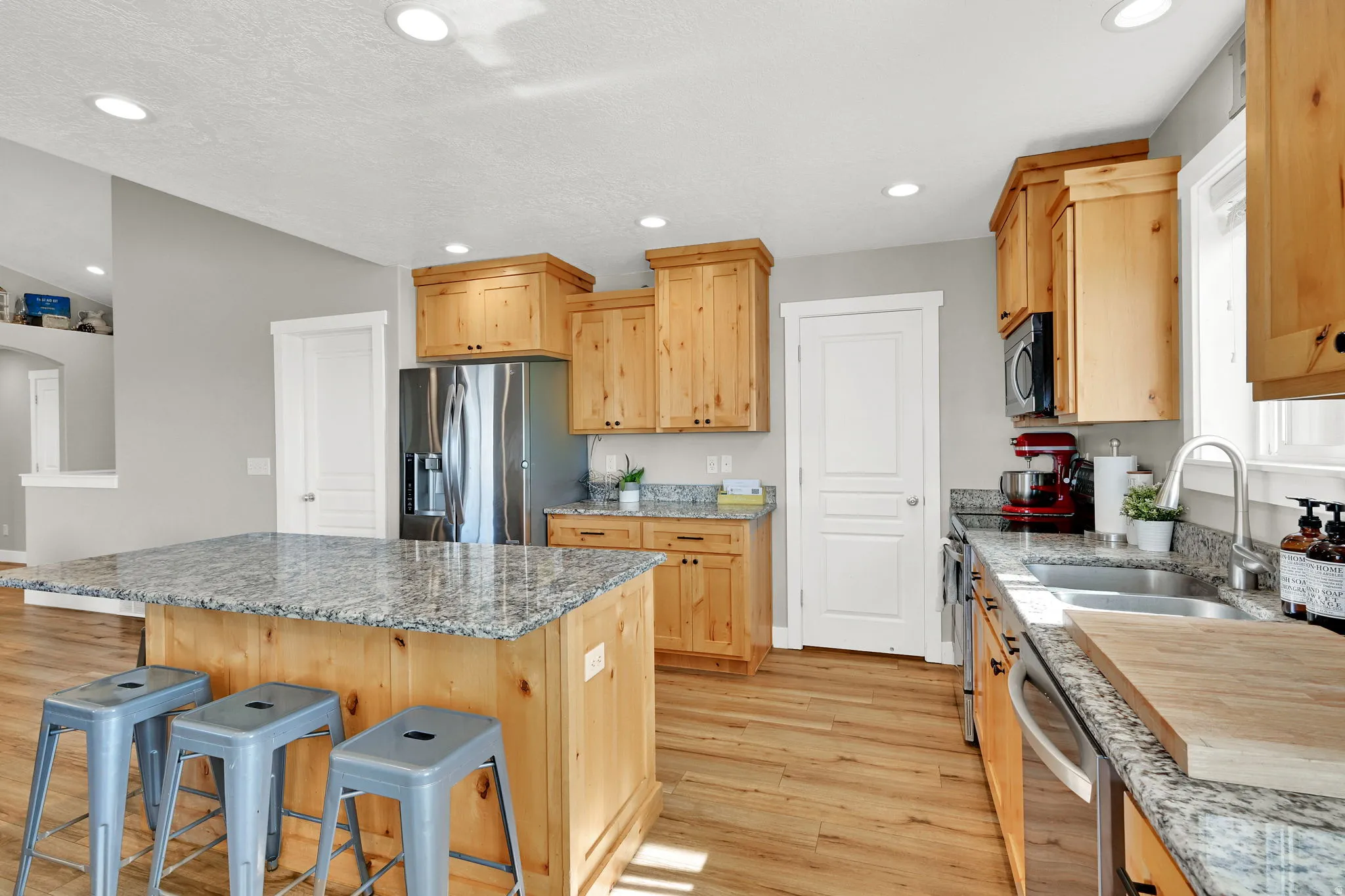Kitchen featuring light wood finish cabinetry, light stone counters, light wood finished floors, stainless steel appliances, and a kitchen island