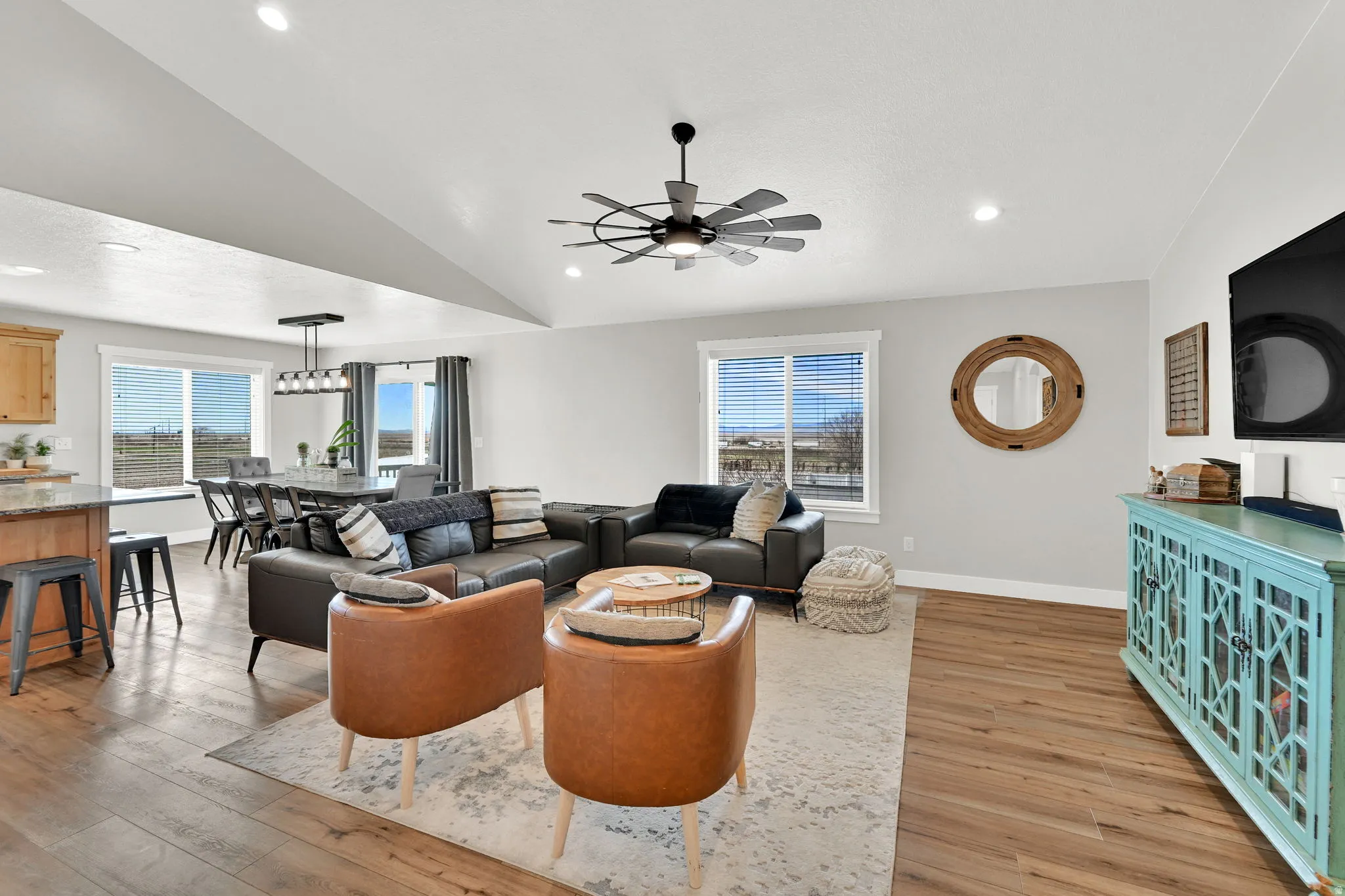 Living room with light wood-style flooring, vaulted ceiling, a ceiling fan, and plenty of natural light