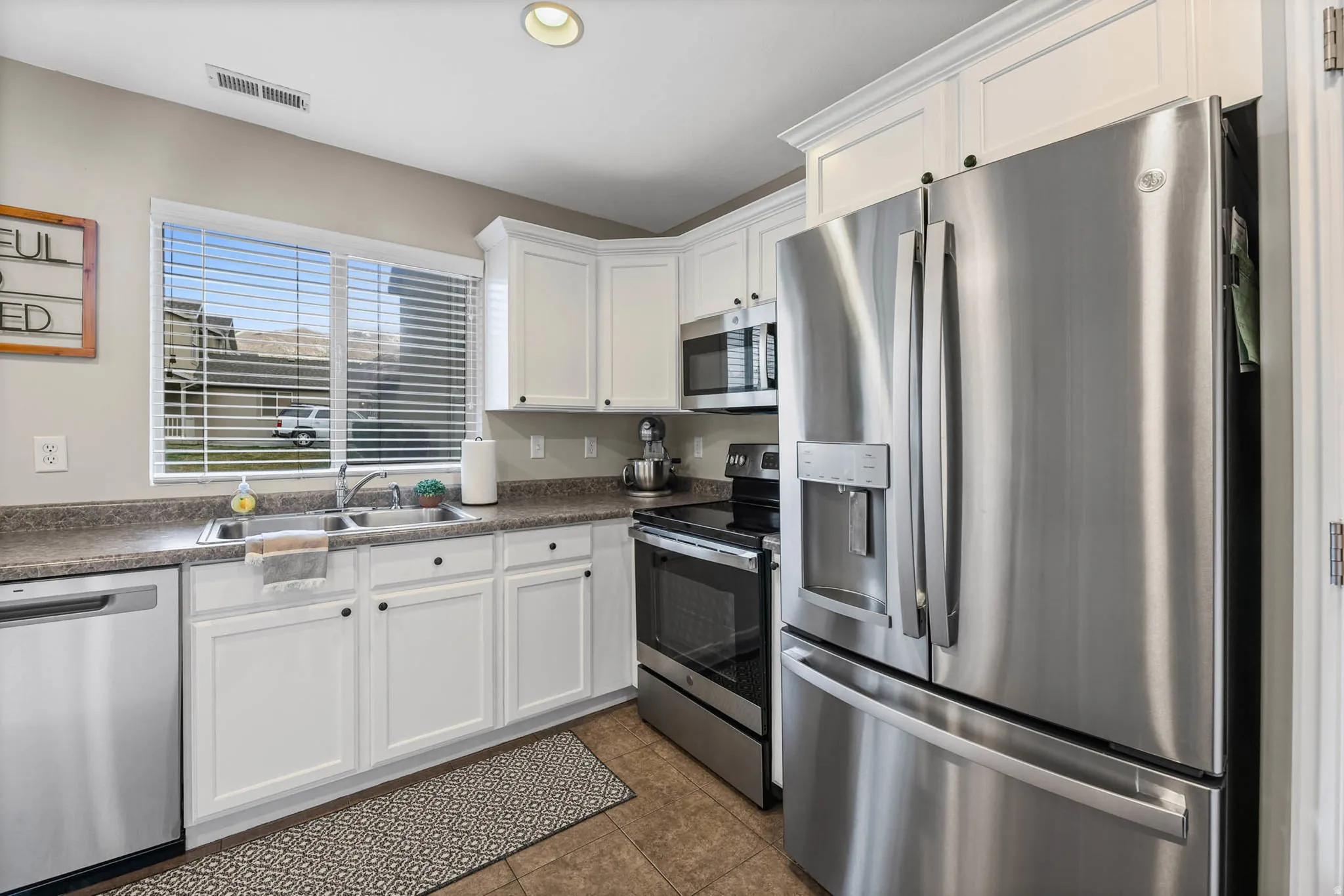 Kitchen with stainless steel appliances, dark countertops, white cabinetry, dark tile patterned flooring, and recessed lighting