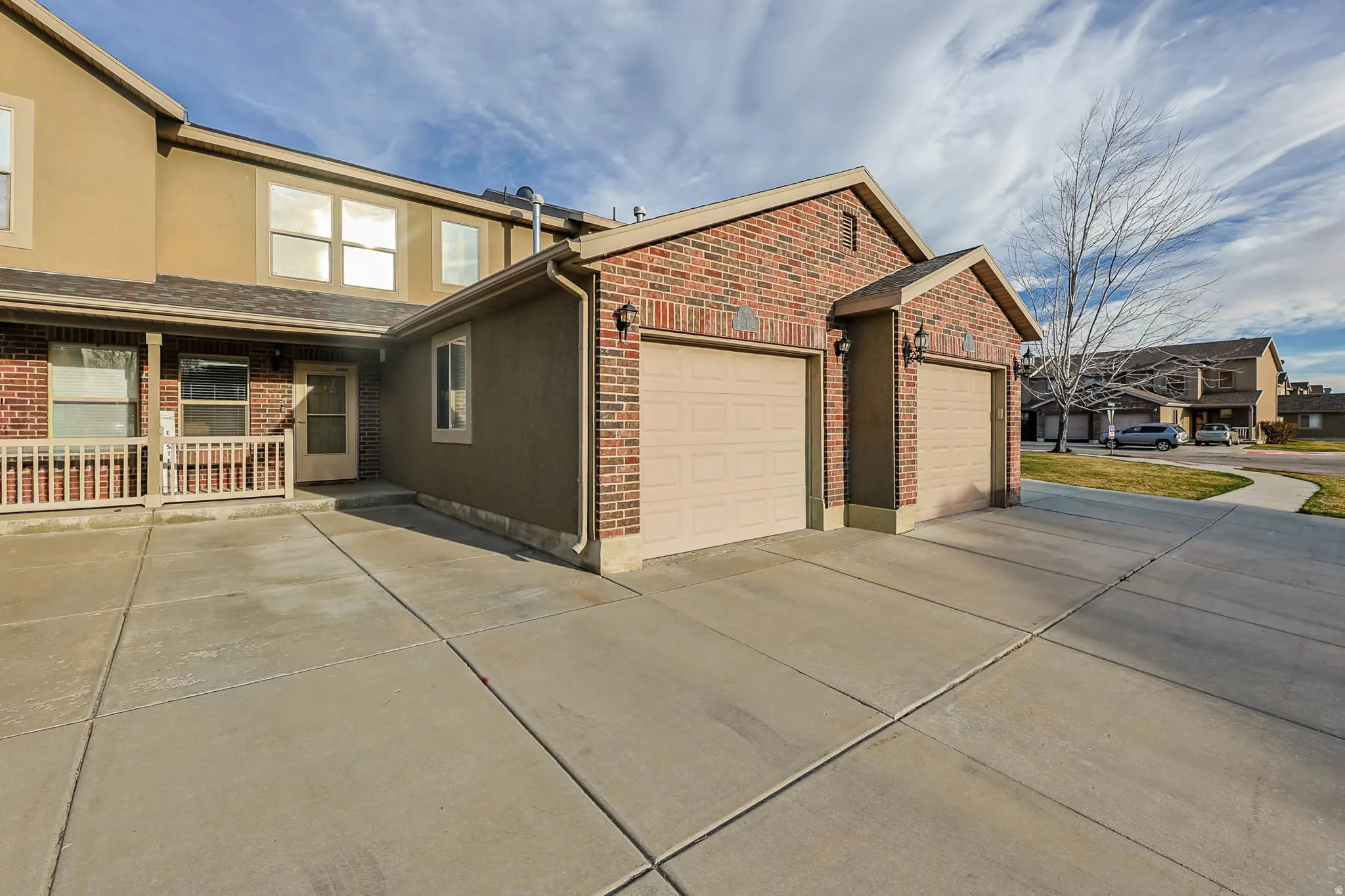 View of side of home with driveway, an attached garage, brick siding, stucco siding, and a patio