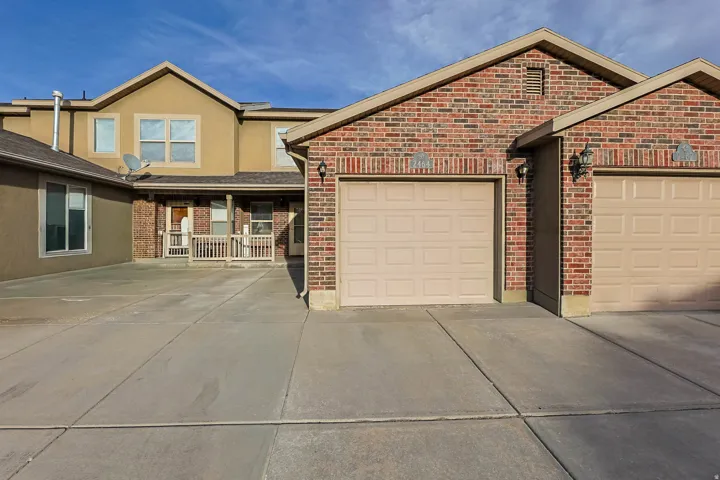 View of front of house featuring driveway, an attached garage, brick siding, and a porch