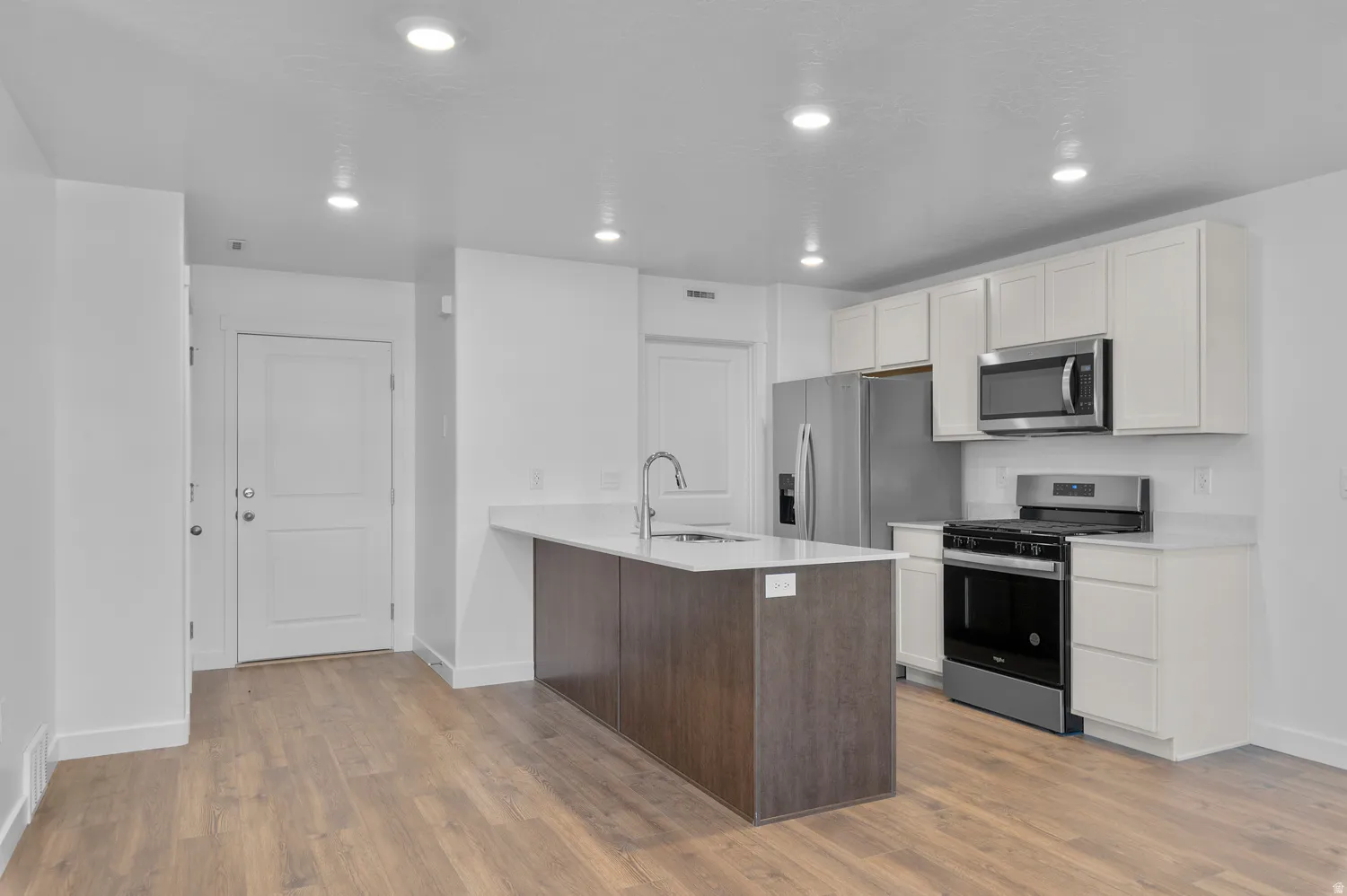 Kitchen with stainless steel appliances, a peninsula, dark wood finished floors, recessed lighting, and white cabinets