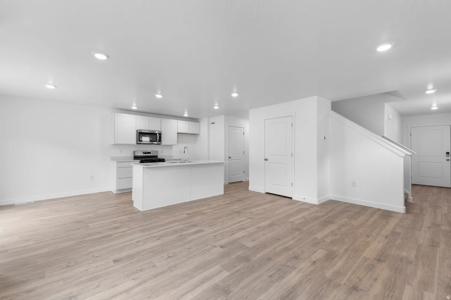 Kitchen with open floor plan, light countertops, white cabinets, stainless steel appliances, and light wood-style flooring