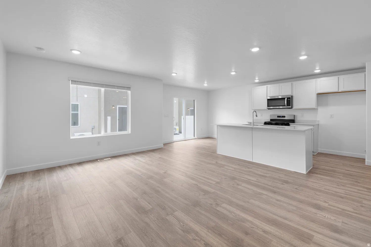 Kitchen with white cabinets, open floor plan, light wood finished floors, an island with sink, and stainless steel appliances