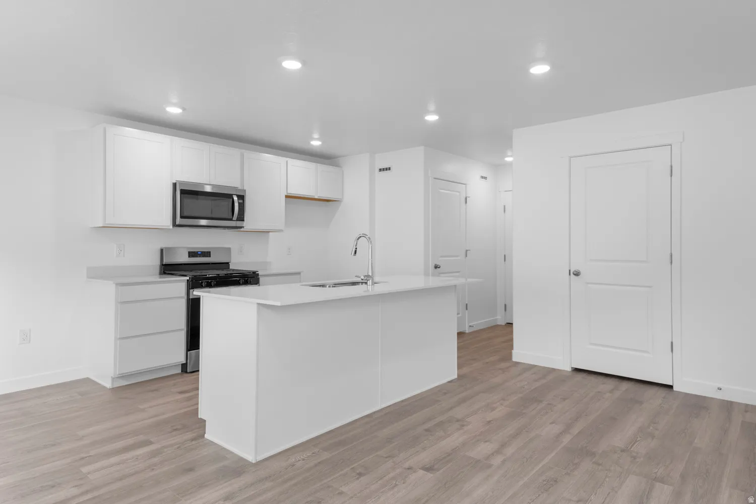 Kitchen with stainless steel appliances, white cabinetry, a center island with sink, light wood-type flooring, and recessed lighting