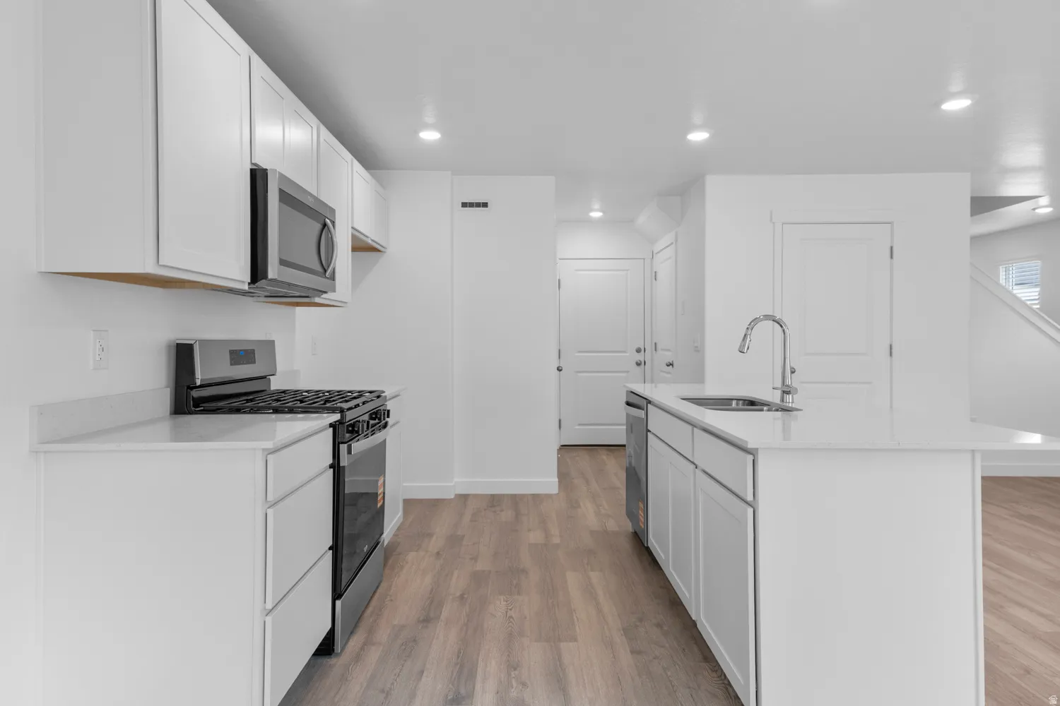 Kitchen with white cabinets, stainless steel appliances, light wood-style flooring, an island with sink, and recessed lighting