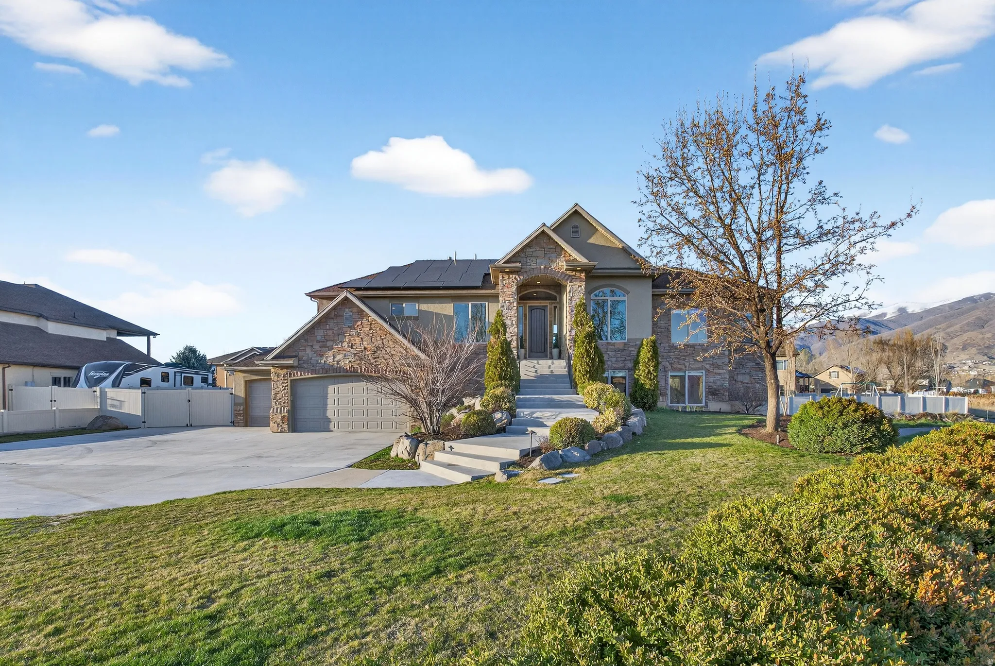 Craftsman-style home featuring stone siding, roof mounted solar panels, a garage, driveway, and a mountain view