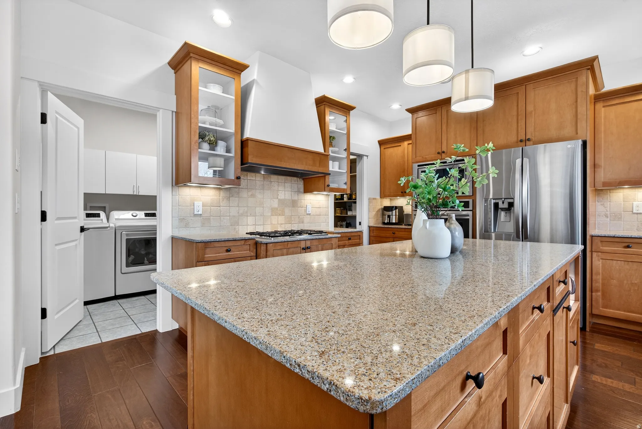 Kitchen with light stone counters, a center island, dark wood-type flooring, and glass insert cabinets