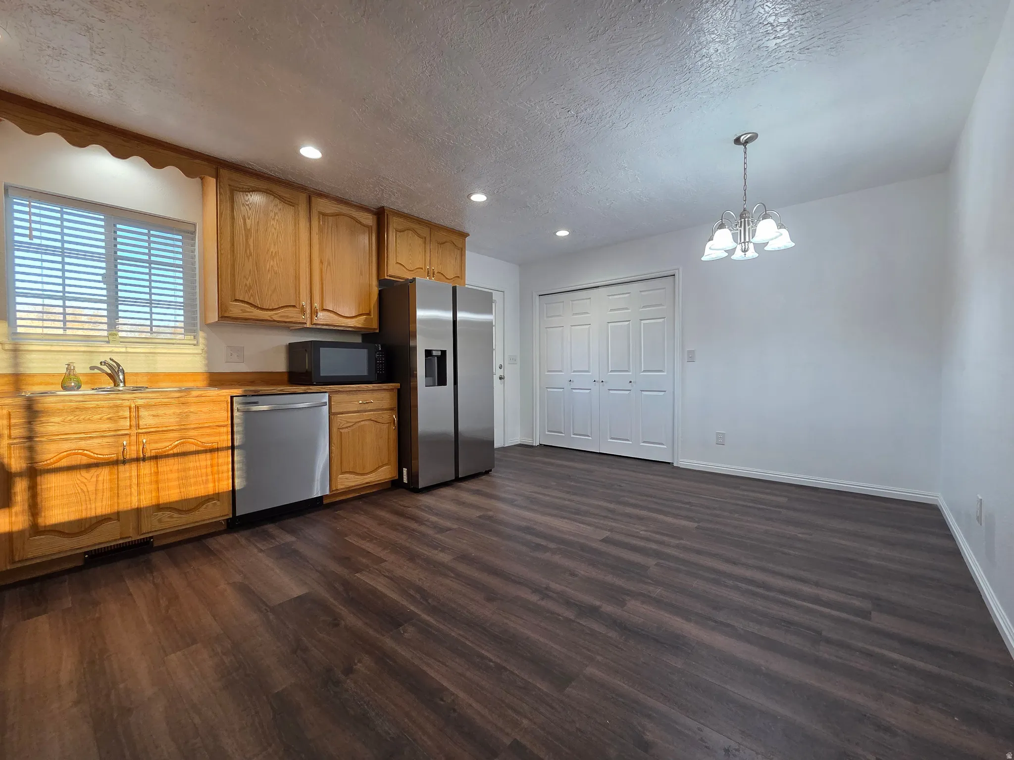 Kitchen featuring stainless steel appliances, hanging lights, dark wood finished floors, a textured ceiling, and wood finish cabinetry