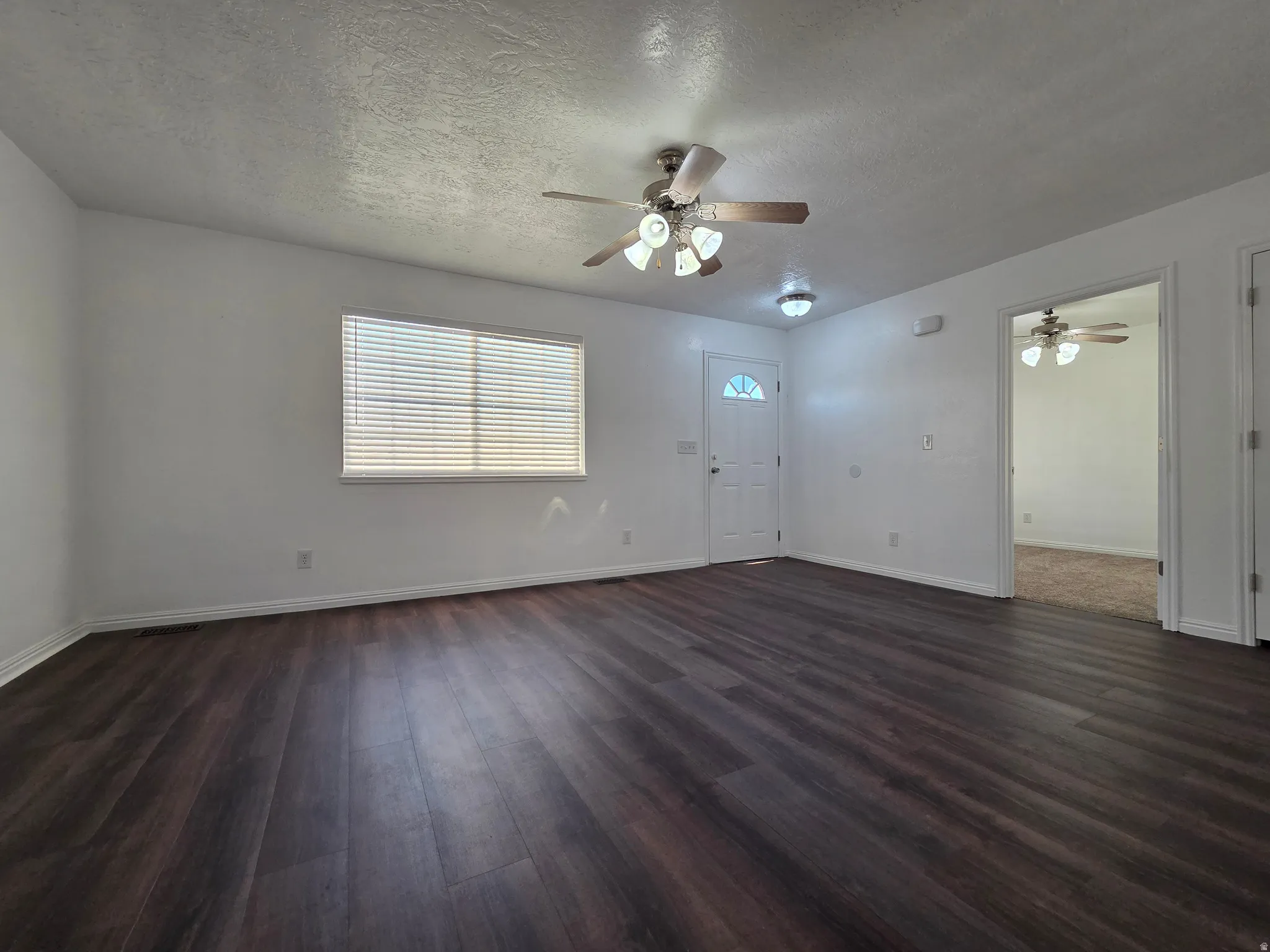 Unfurnished living room featuring a ceiling fan, dark wood finished floors, and a textured ceiling