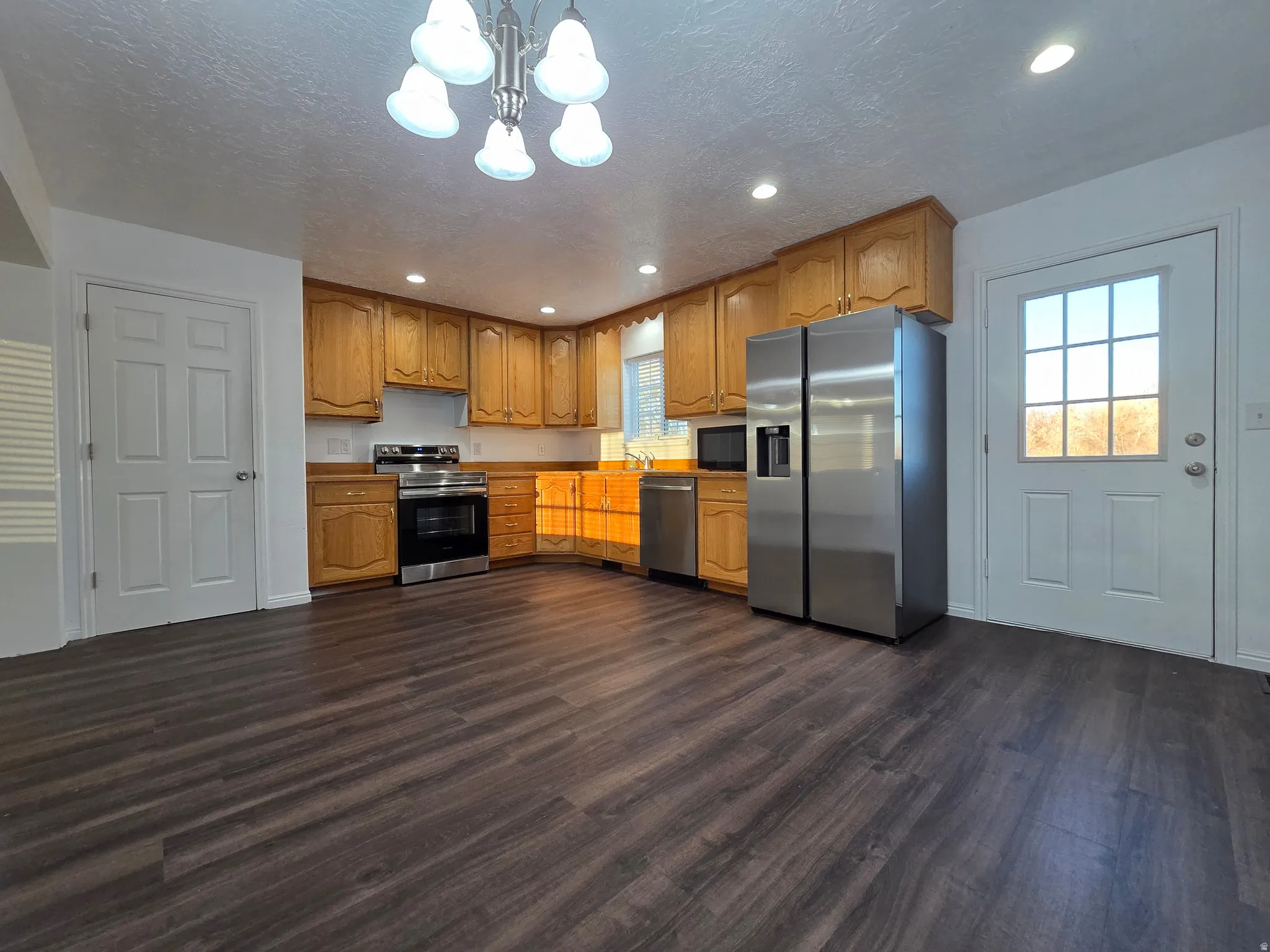 Kitchen with stainless steel appliances, dark wood-style flooring, wood finish cabinets, a chandelier, and a textured ceiling