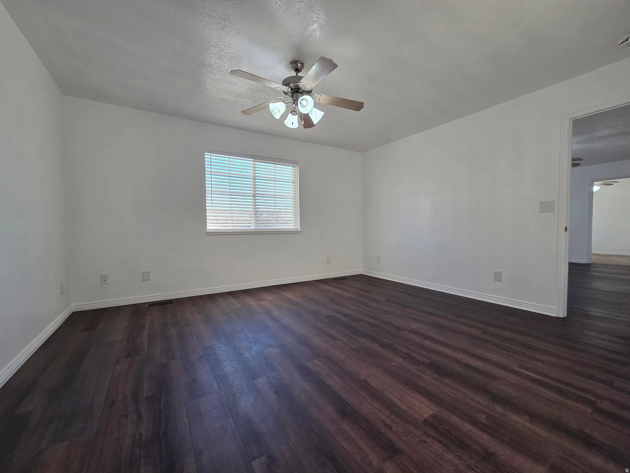 Unfurnished room featuring ceiling fan, dark wood-type flooring, and a textured ceiling