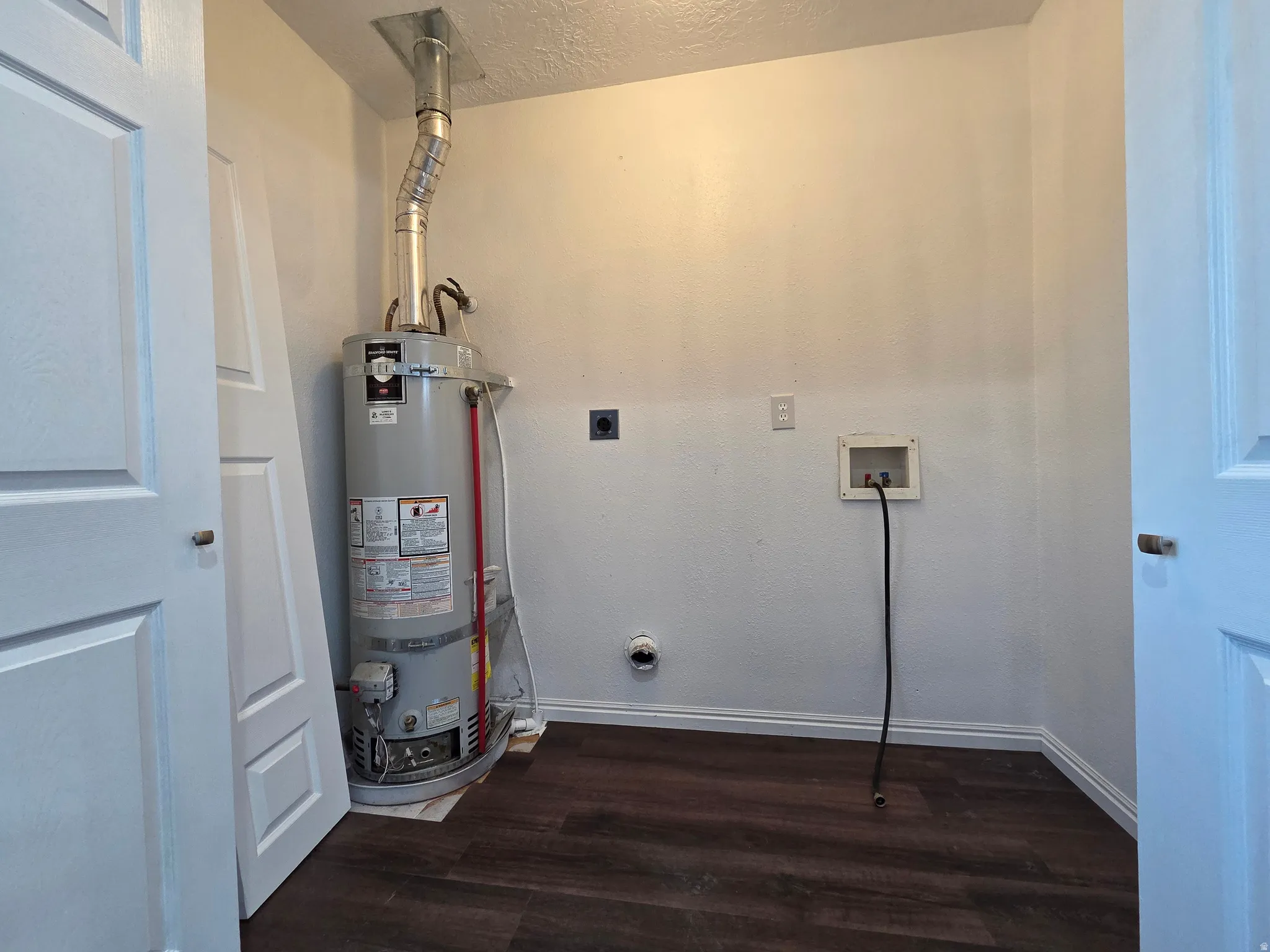 Laundry area featuring dark wood-style flooring, secured water heater, a textured ceiling, hookup for an electric dryer, and hookup for a washing machine